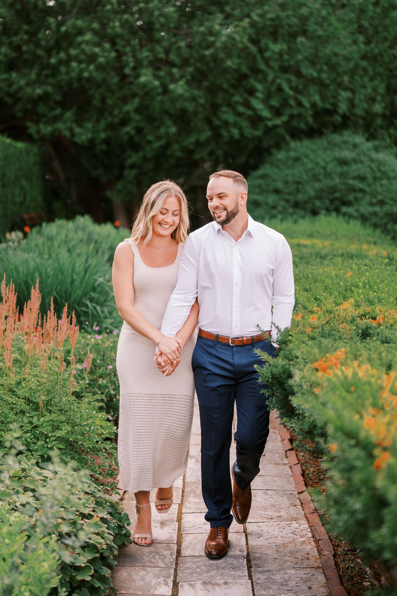 A couple walks hand in hand along a garden path surrounded by colorful summer blooms and lush greenery.