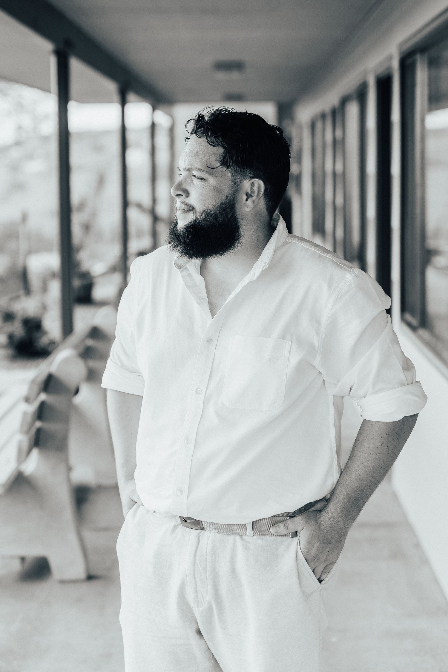 Person in white attire standing on a covered porch with hands in pockets.