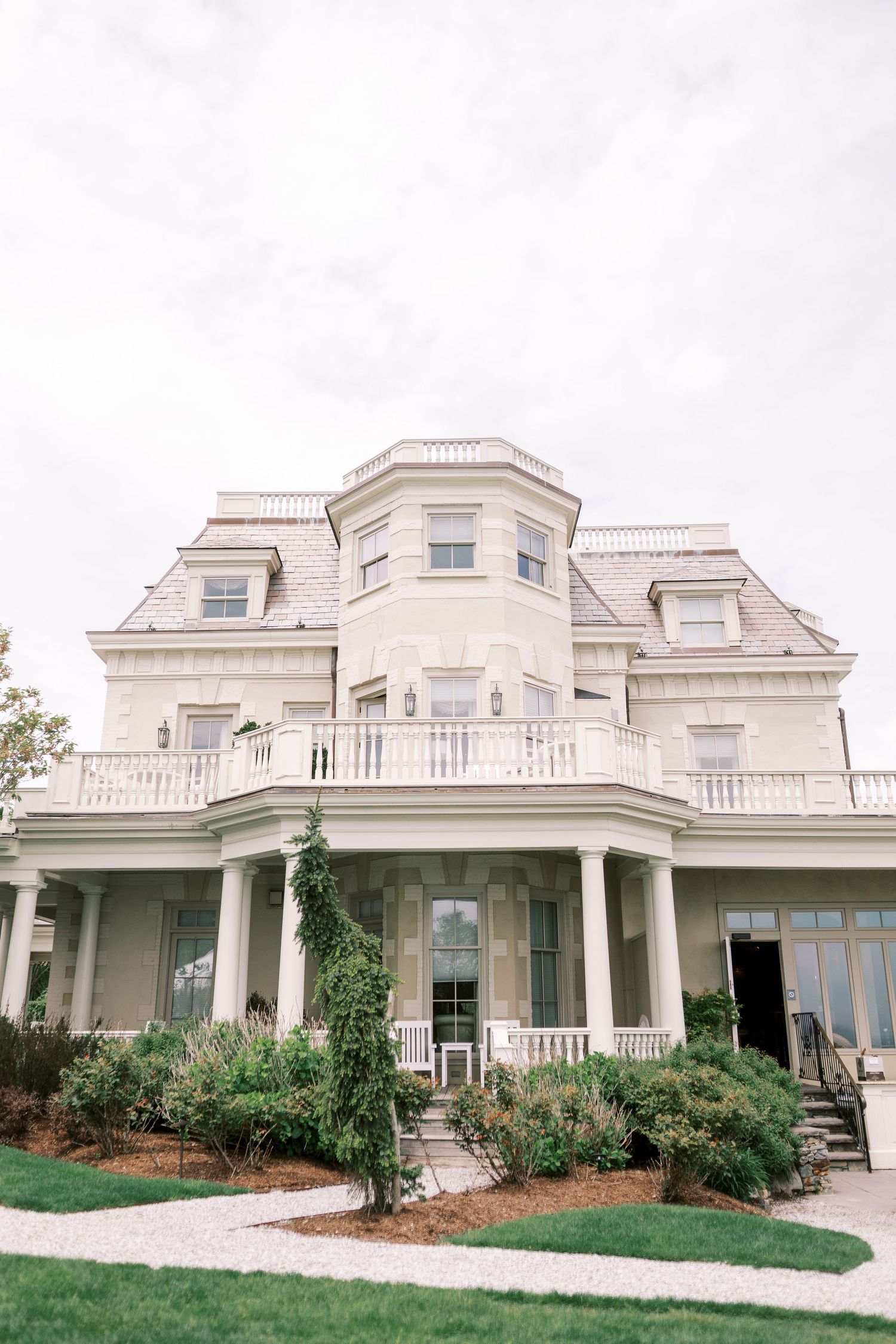 Elegant white mansion featuring multiple bay windows, dormer windows, and wraparound porch with classical columns.