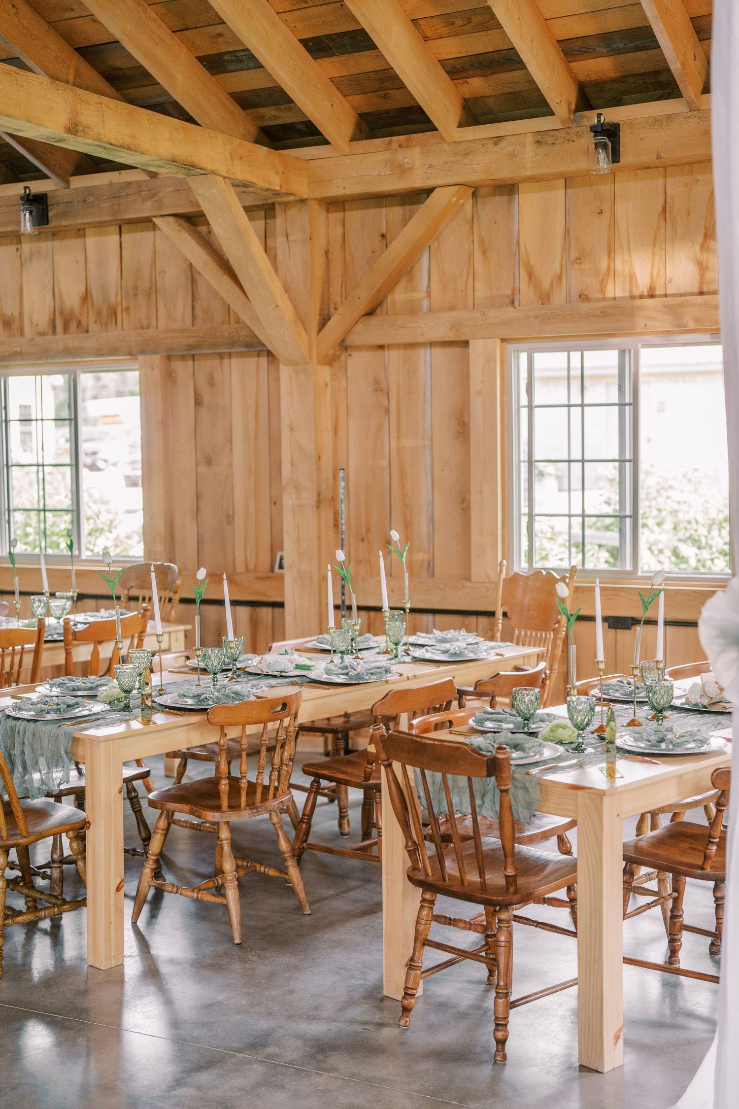 Rustic wooden barn interior set up for dining with long tables and chairs decorated with soft blue table settings.