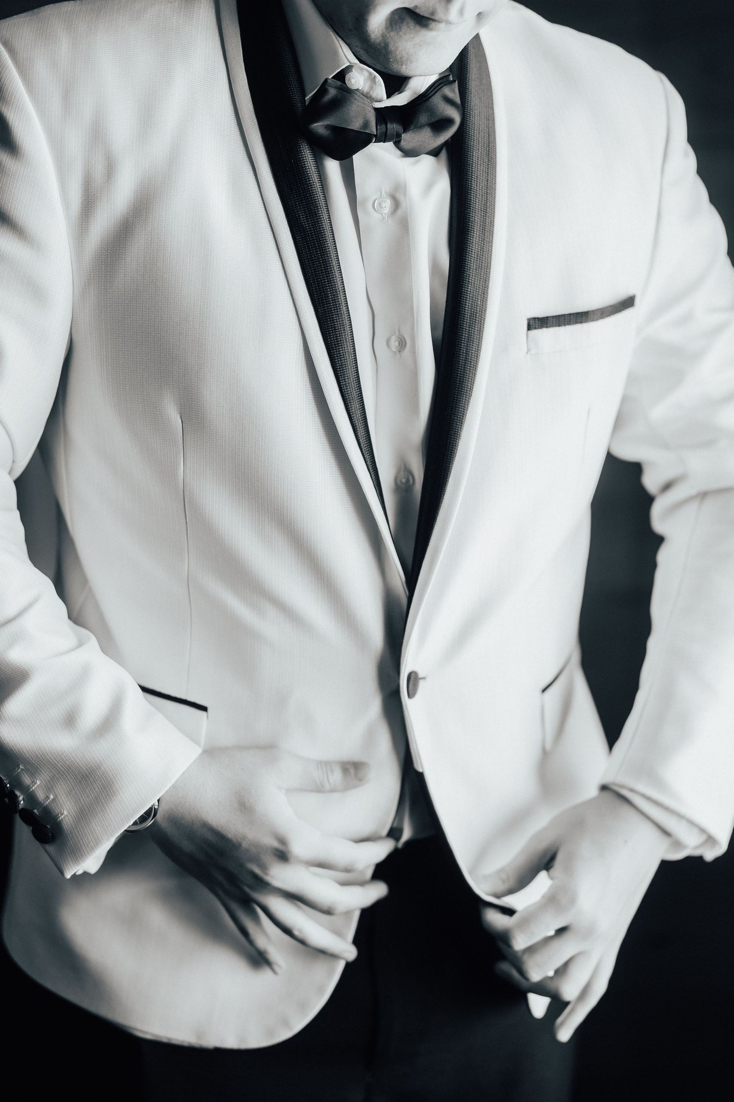 Close-up of a crisp white tuxedo jacket with black bow tie and trim details against dark background.