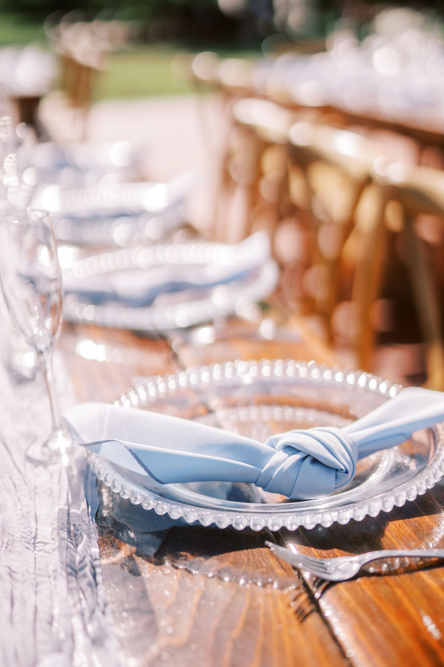 Elegant place setting with light blue knotted napkin on a white scalloped plate at rustic wooden table.