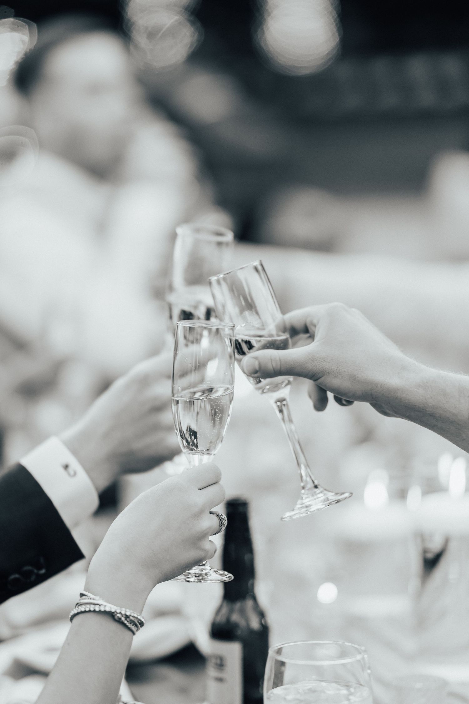 Hands raise champagne glasses in a celebratory toast at an elegant event with bokeh lighting in the background.