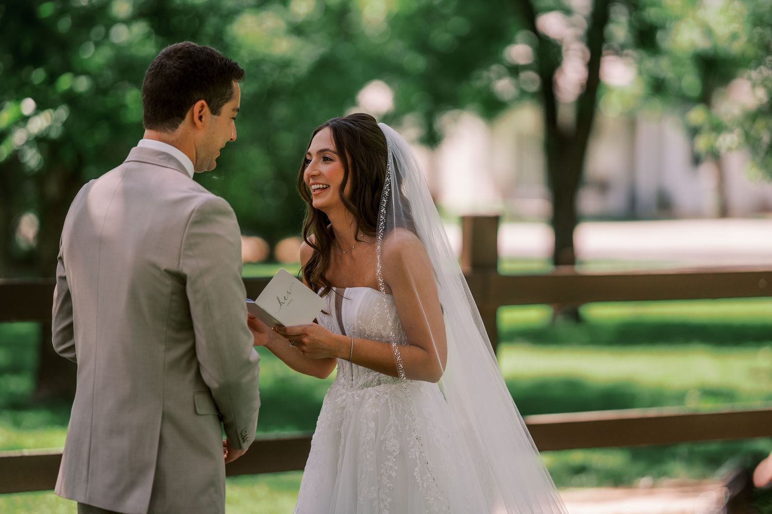 A bride and groom share a joyful moment together in a park with lush green trees in the background.