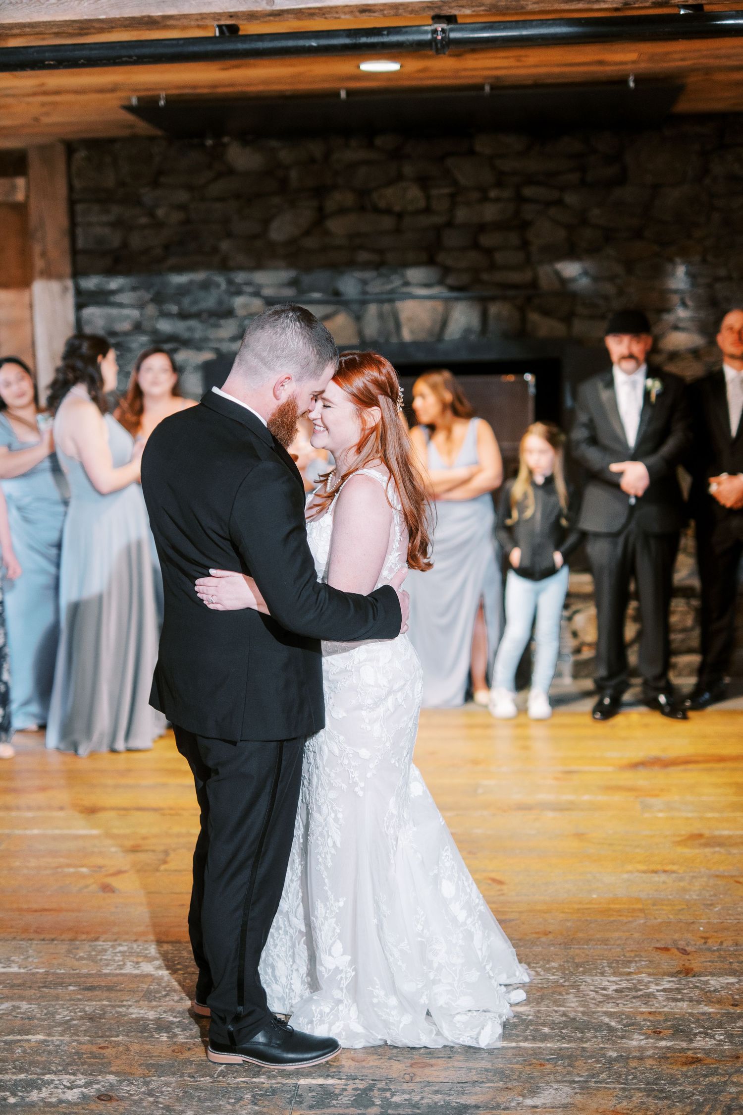 A romantic first dance at a rustic stone venue with guests watching in the background.