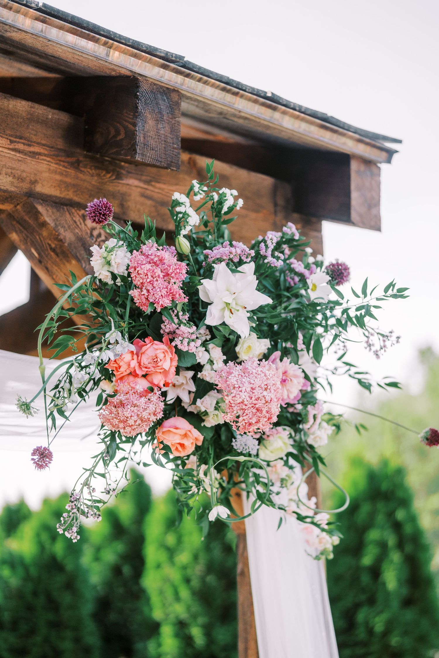 Lush floral arrangement with pink and white blooms decorating a wooden wedding arch.