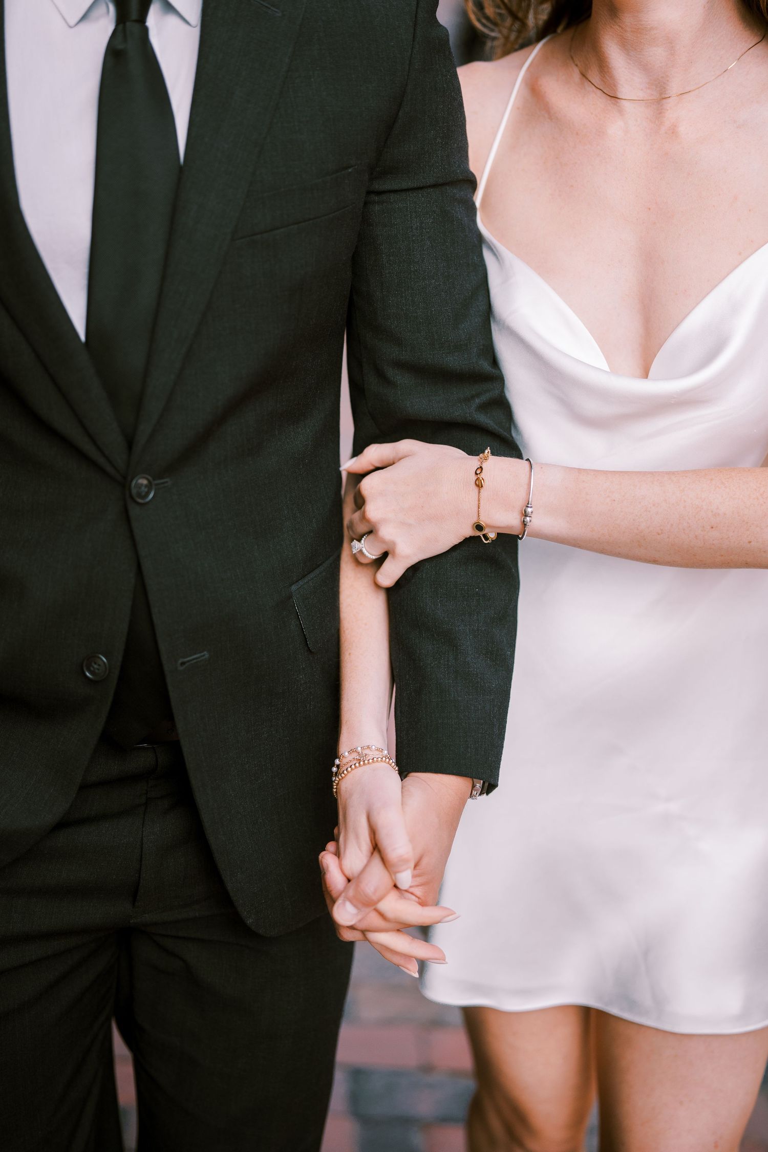 Close-up view of elegant hands with delicate jewelry against black and white formalwear during a romantic moment.