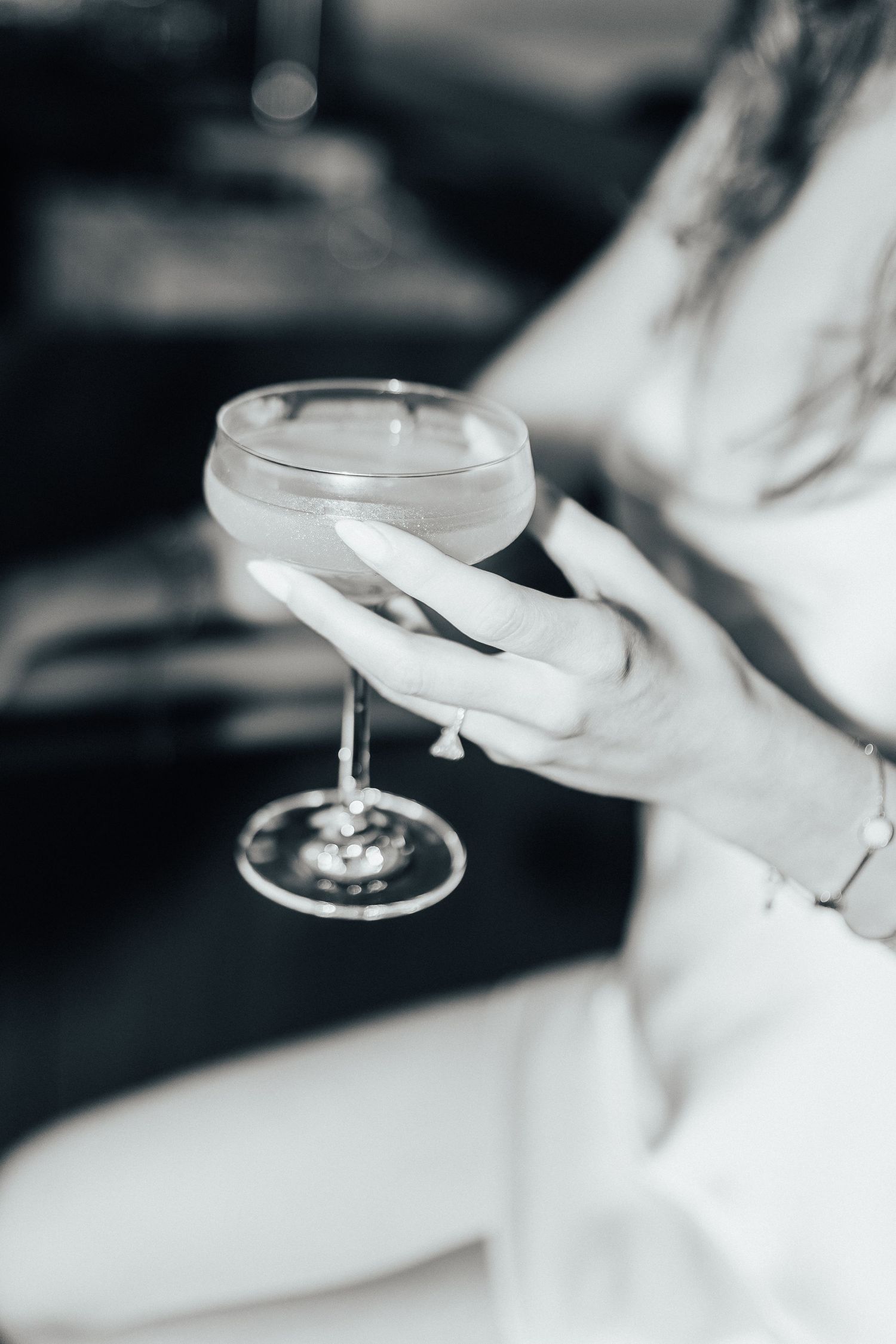 An elegant hand holds a delicate coupe glass containing a classic cocktail in a black and white artistic style.