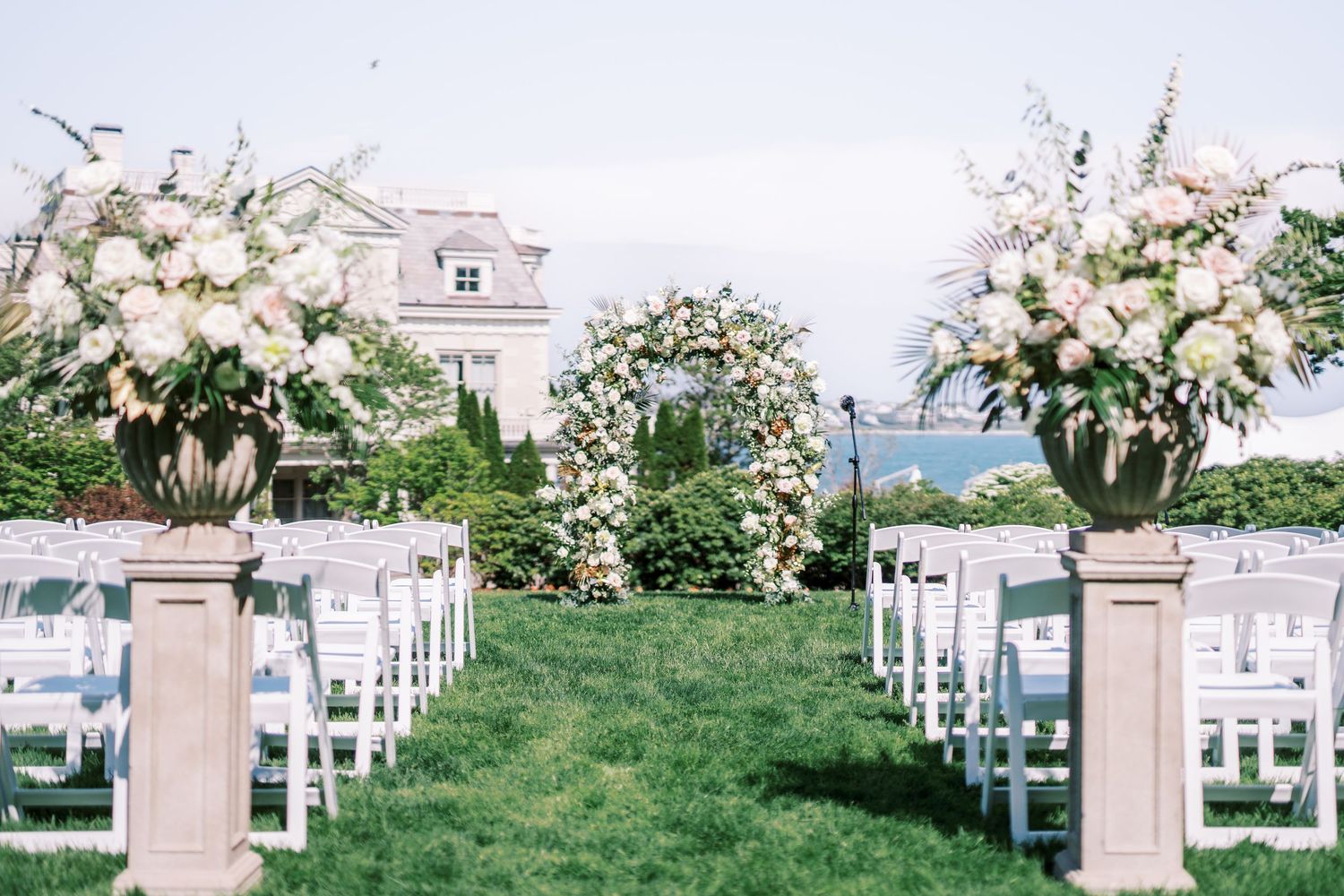Elegant outdoor wedding ceremony setup with white chairs and floral arrangements leading to an arch overlooking the ocean.