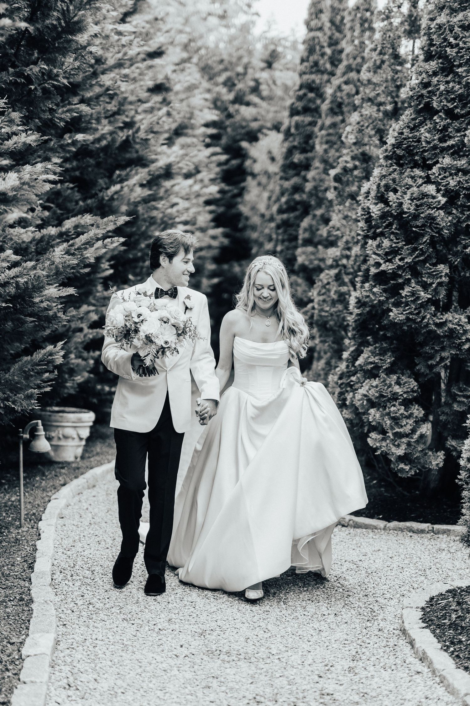 Beautiful couple walking down a white gravel path in a lush garden setting during their wedding ceremony.