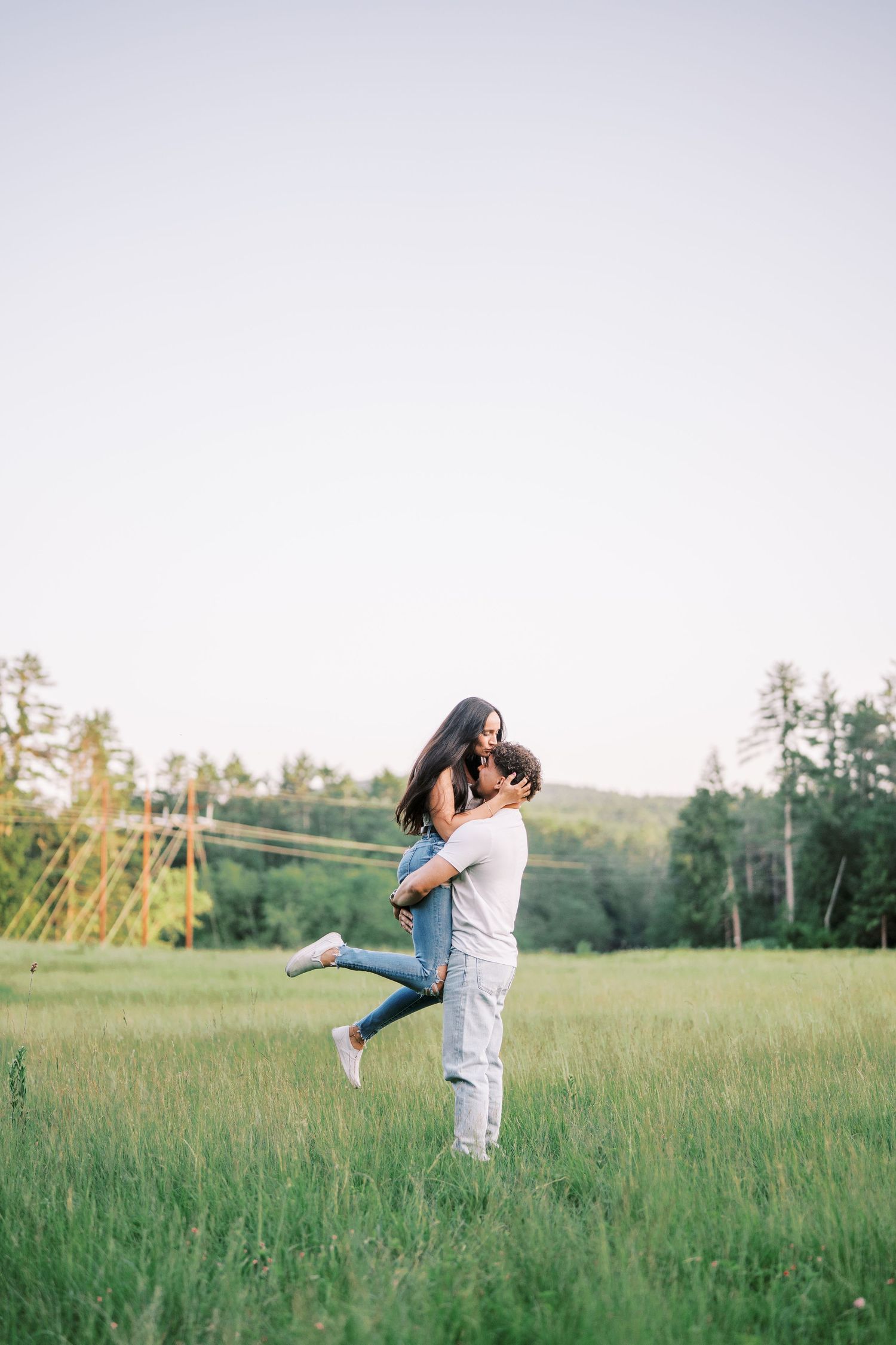 A couple embraces in a sunny meadow as one person lifts the other off the ground.