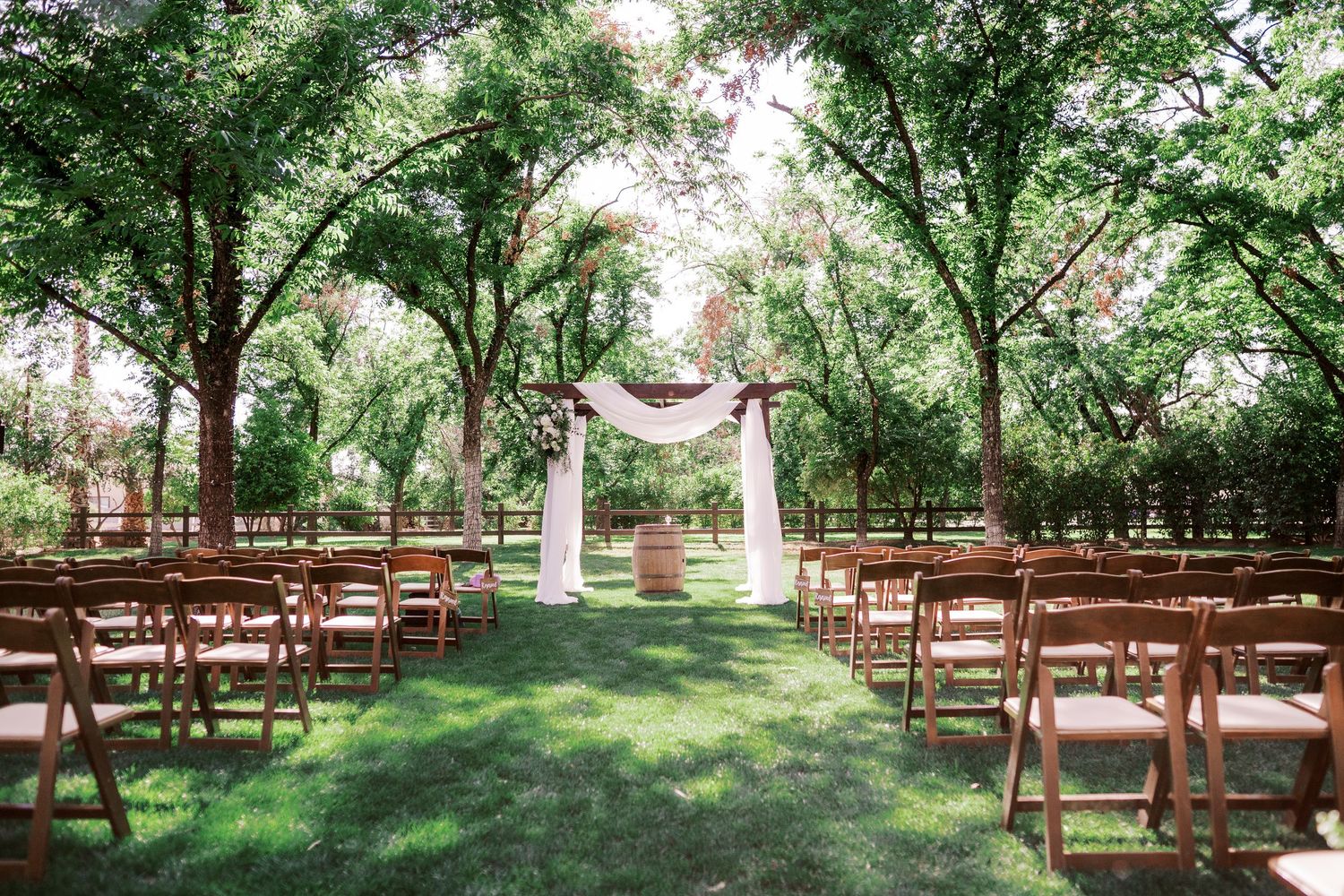 Wooden benches arranged in rows under towering trees create a serene outdoor ceremony space in a natural woodland setting.