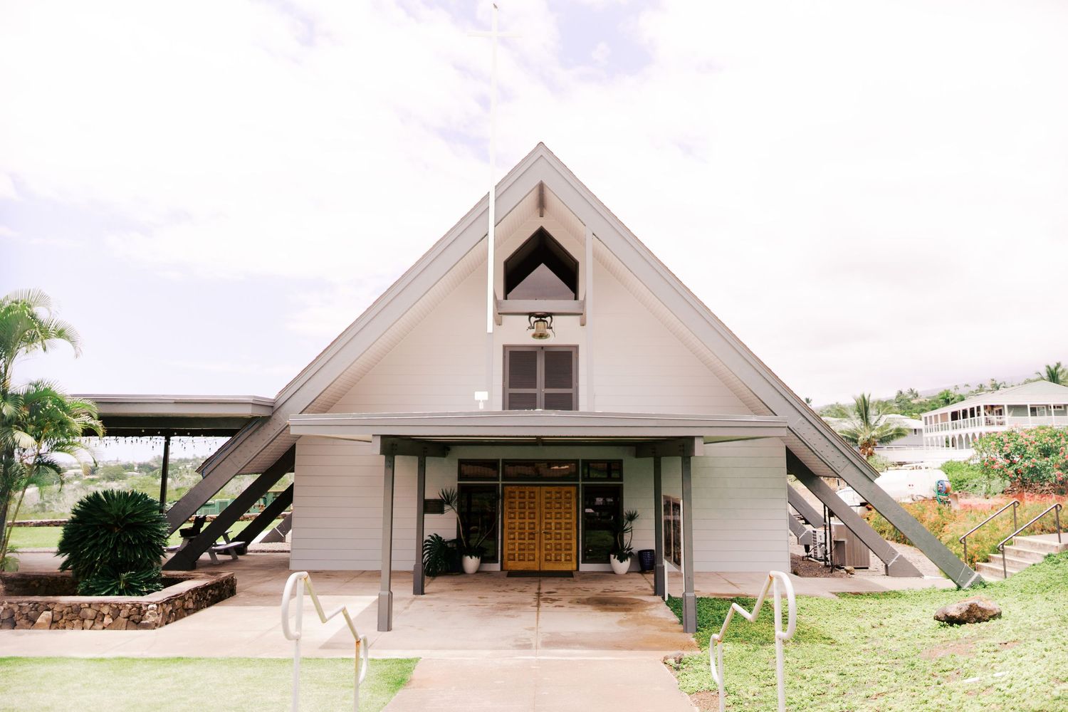 A modern A-frame church building with unique architectural design and palm trees.