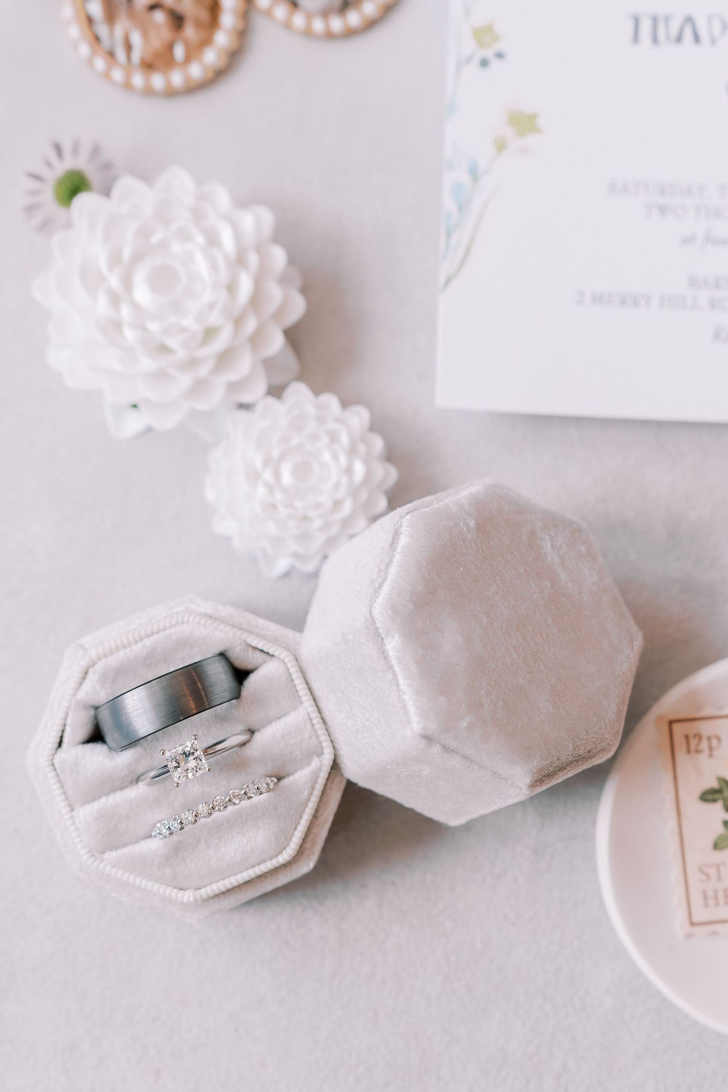 Elegant white octagonal ring boxes with delicate floral decorations displayed alongside wedding rings.