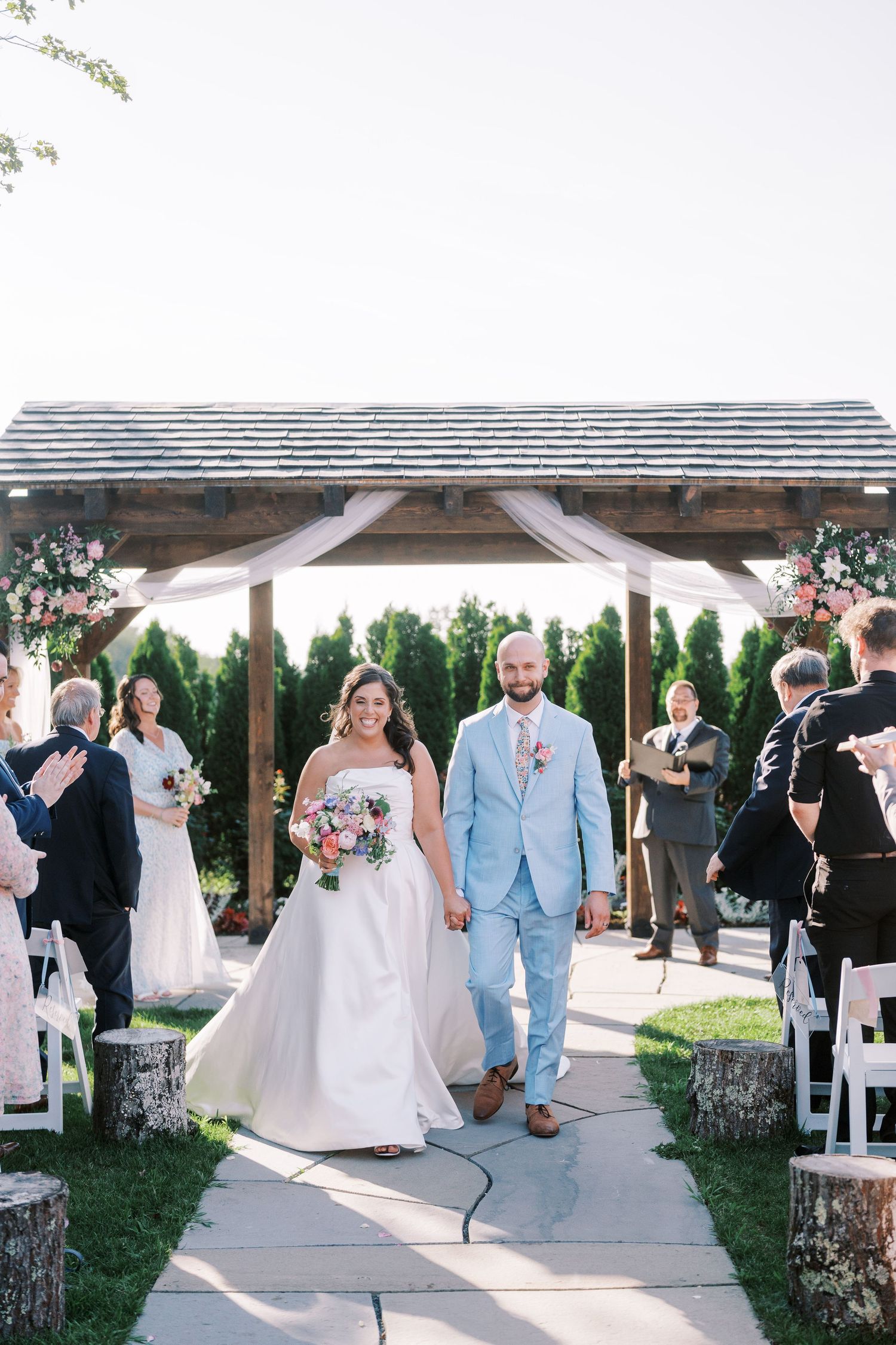 Wedding guests mingling under a covered outdoor reception area with white chairs and rustic decor.