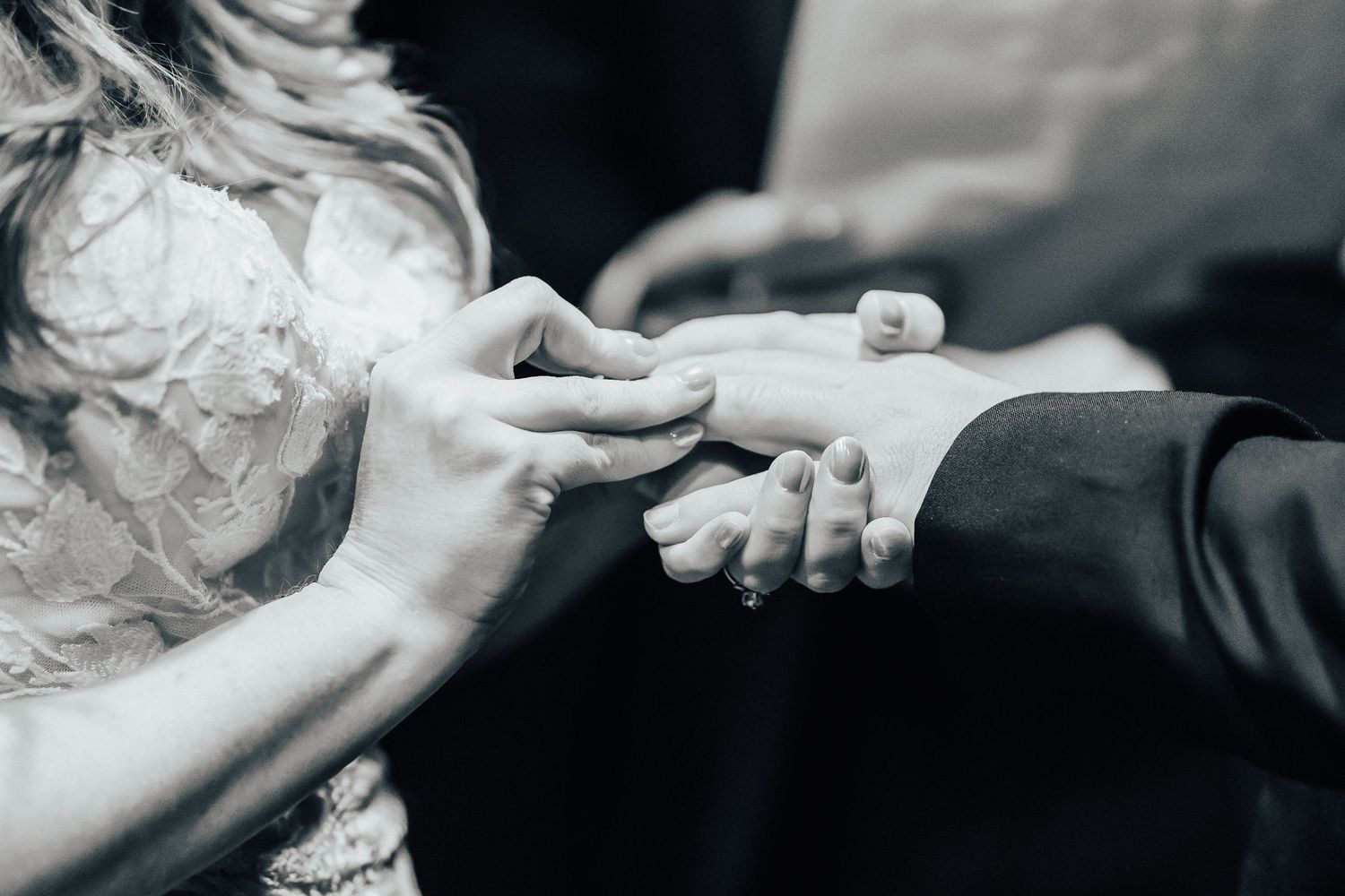 Black and white close-up photo of hands exchanging rings during a wedding ceremony.