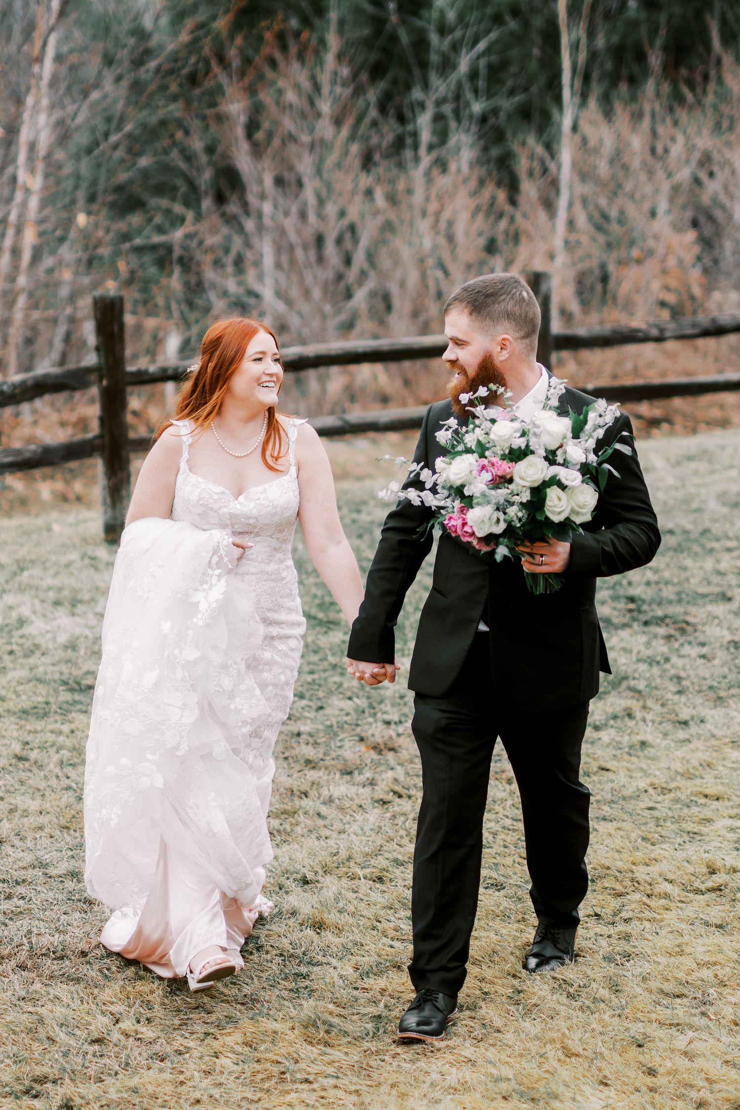 Wedding couple walking along rustic fence with beautiful floral bouquet.