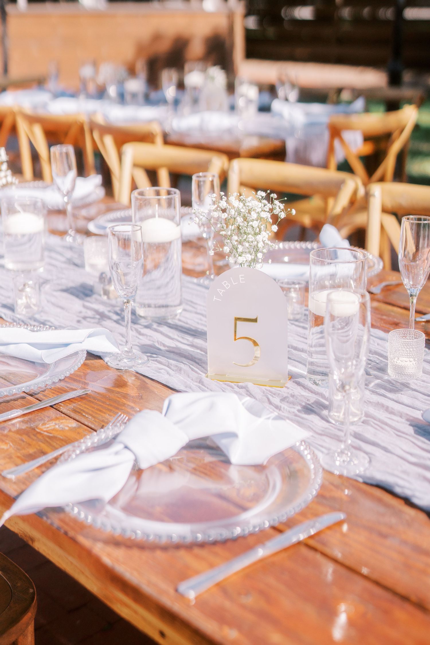 Elegant table setting with gold number 5, rustic wooden tables, and delicate baby's breath centerpiece for a wedding reception.