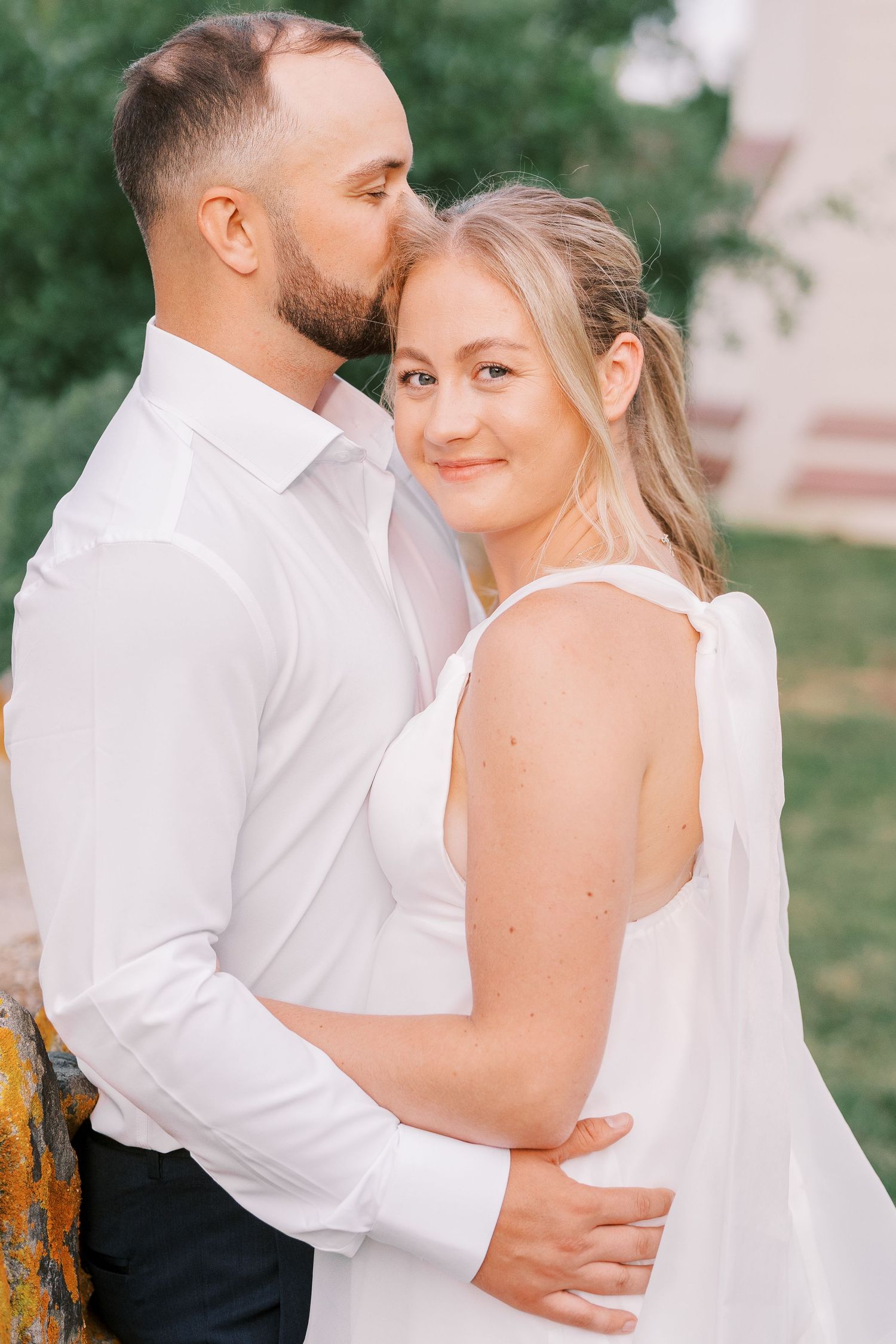 Intimate portrait of couple in white clothing against garden backdrop.