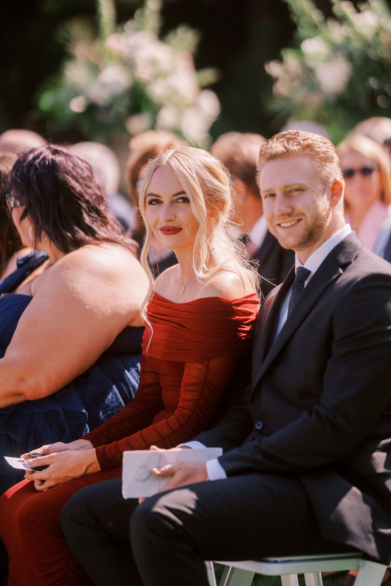 Guests seated in rows at an outdoor ceremony share candid reactions and laughter during a special moment.