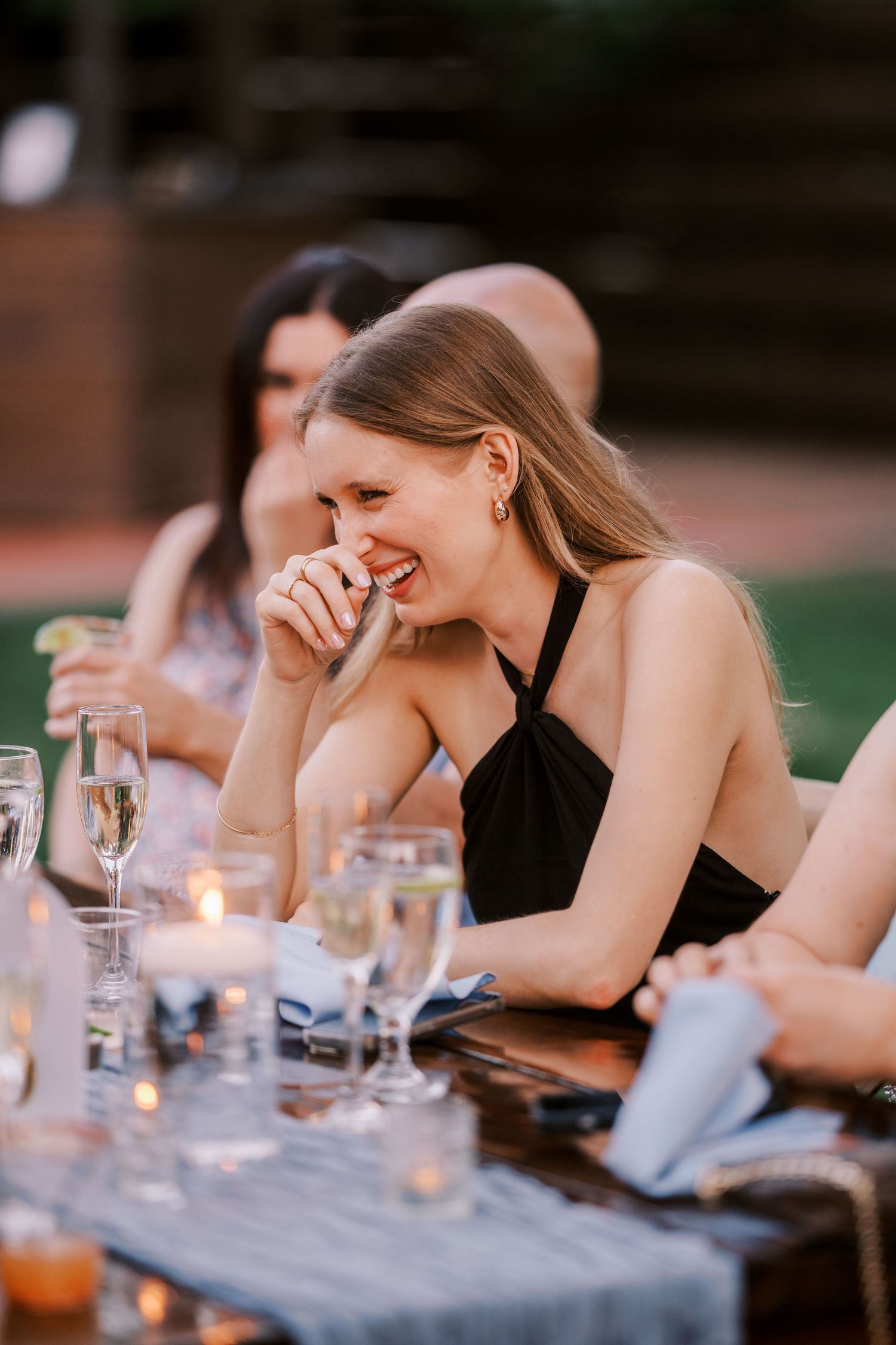 People gathered at a table share laughter and drinks during an evening outdoor dining experience.