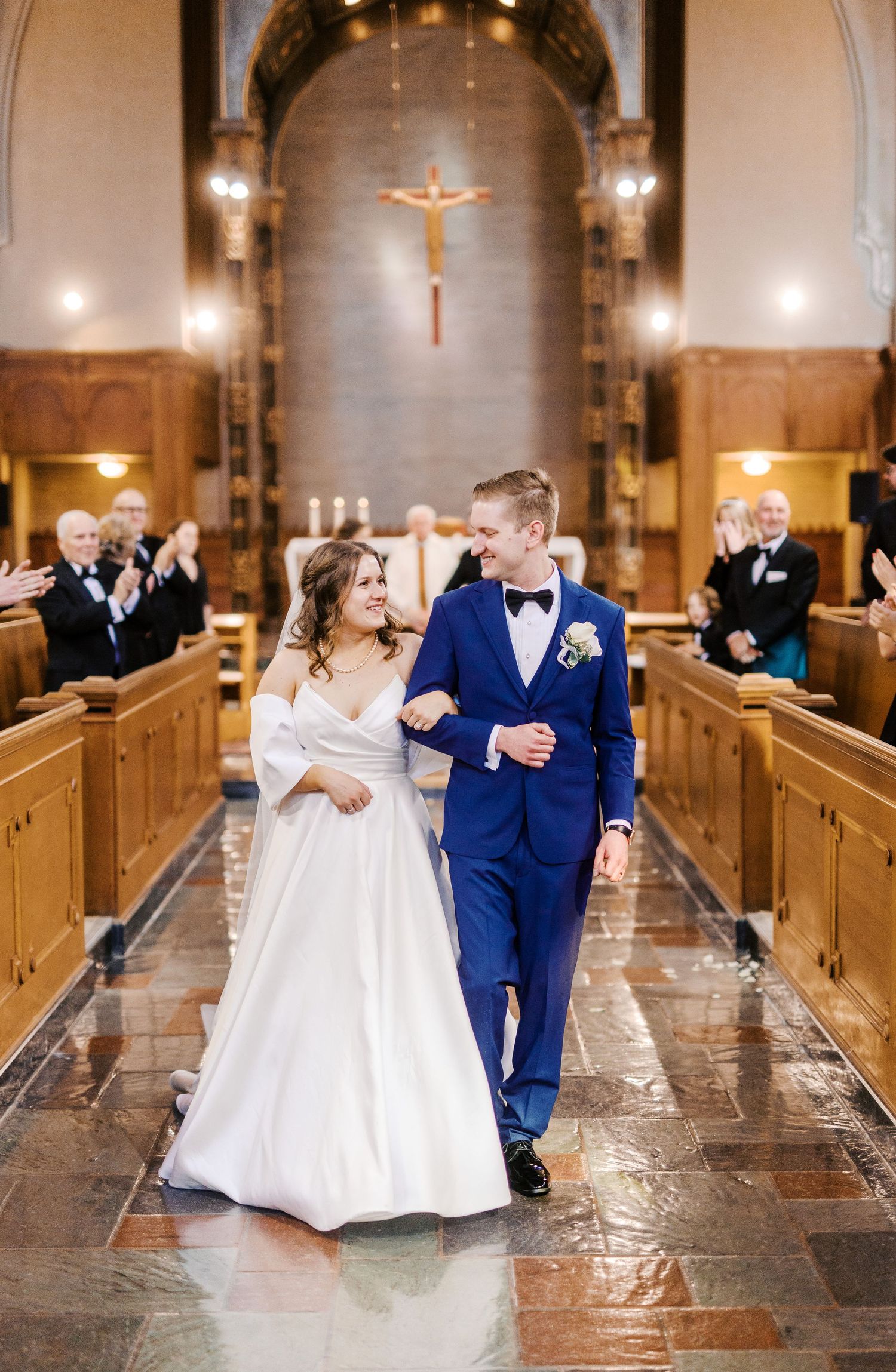 A stunning wedding ceremony exit in a traditional church with illuminated crucifix and wooden pews.
