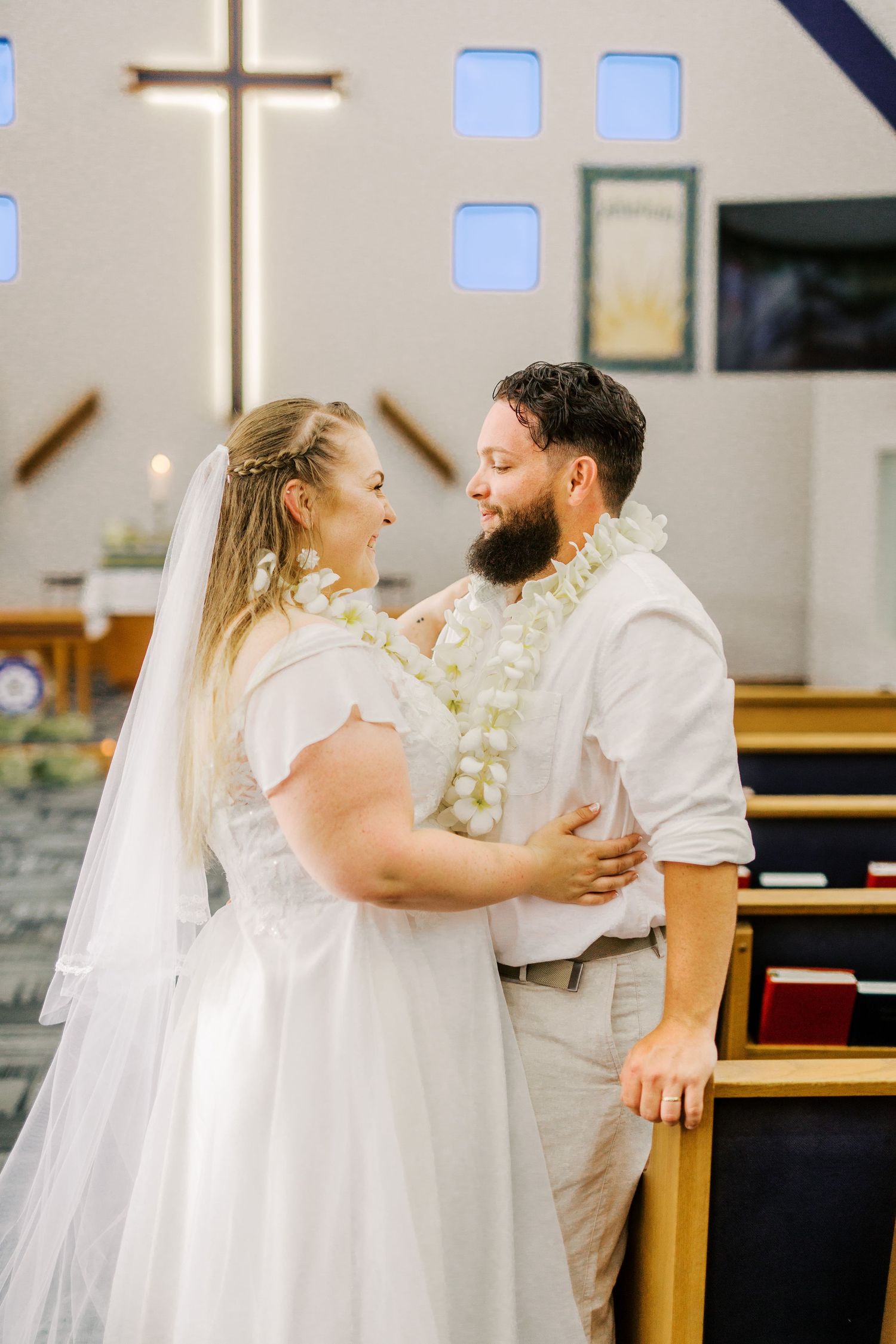 Wedding couple embracing in church sanctuary with illuminated cross in background.
