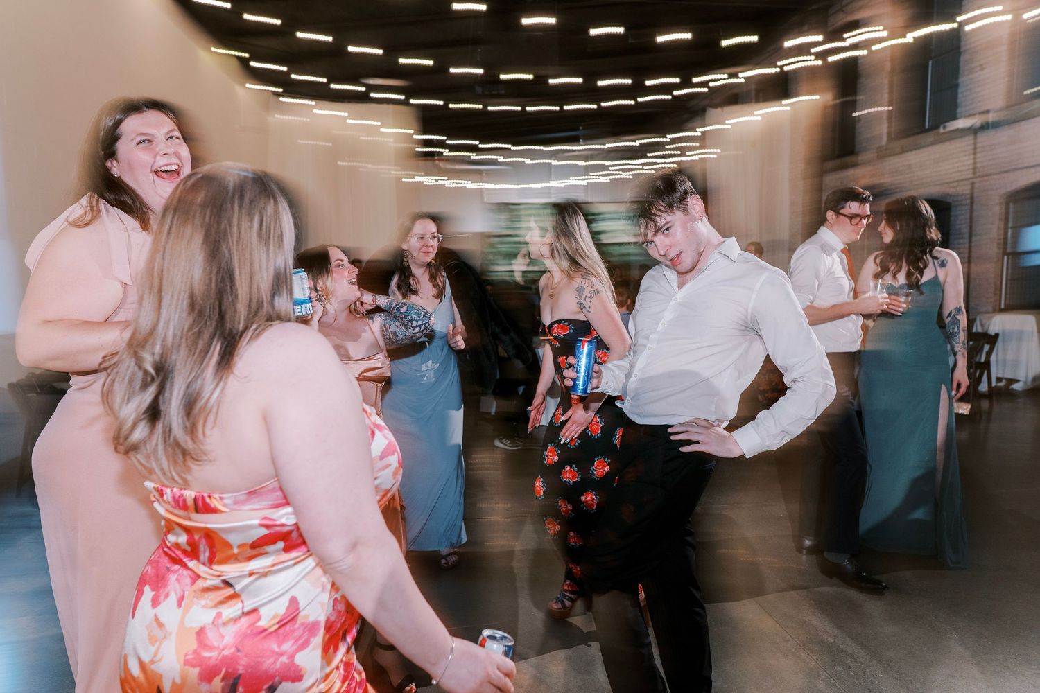 Wedding reception guests dancing and celebrating in a modern venue with overhead lighting.