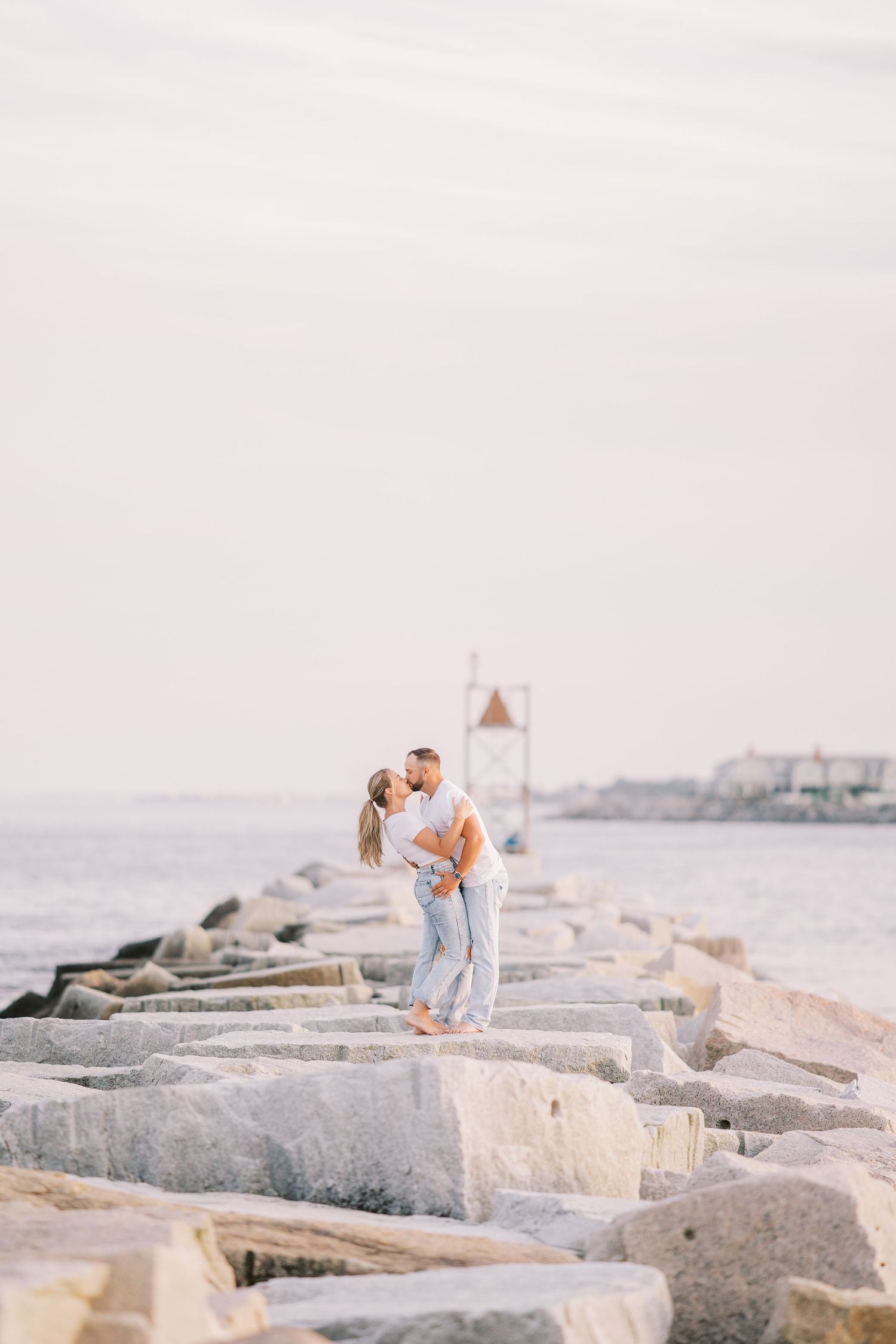 Couple shares intimate moment on rocky coastal breakwater during sunset.