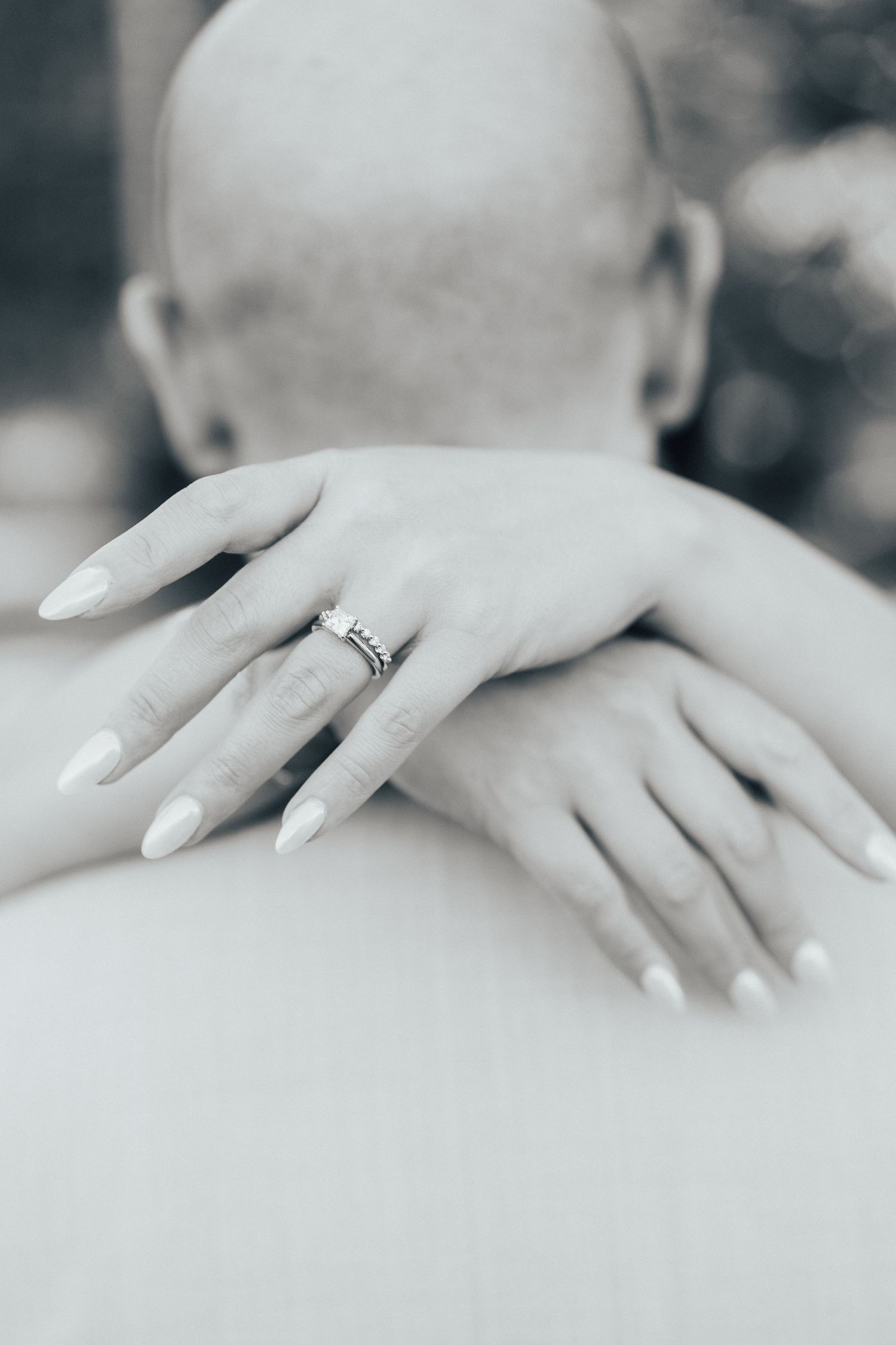 Close-up of hands displaying an elegant engagement ring in black and white.