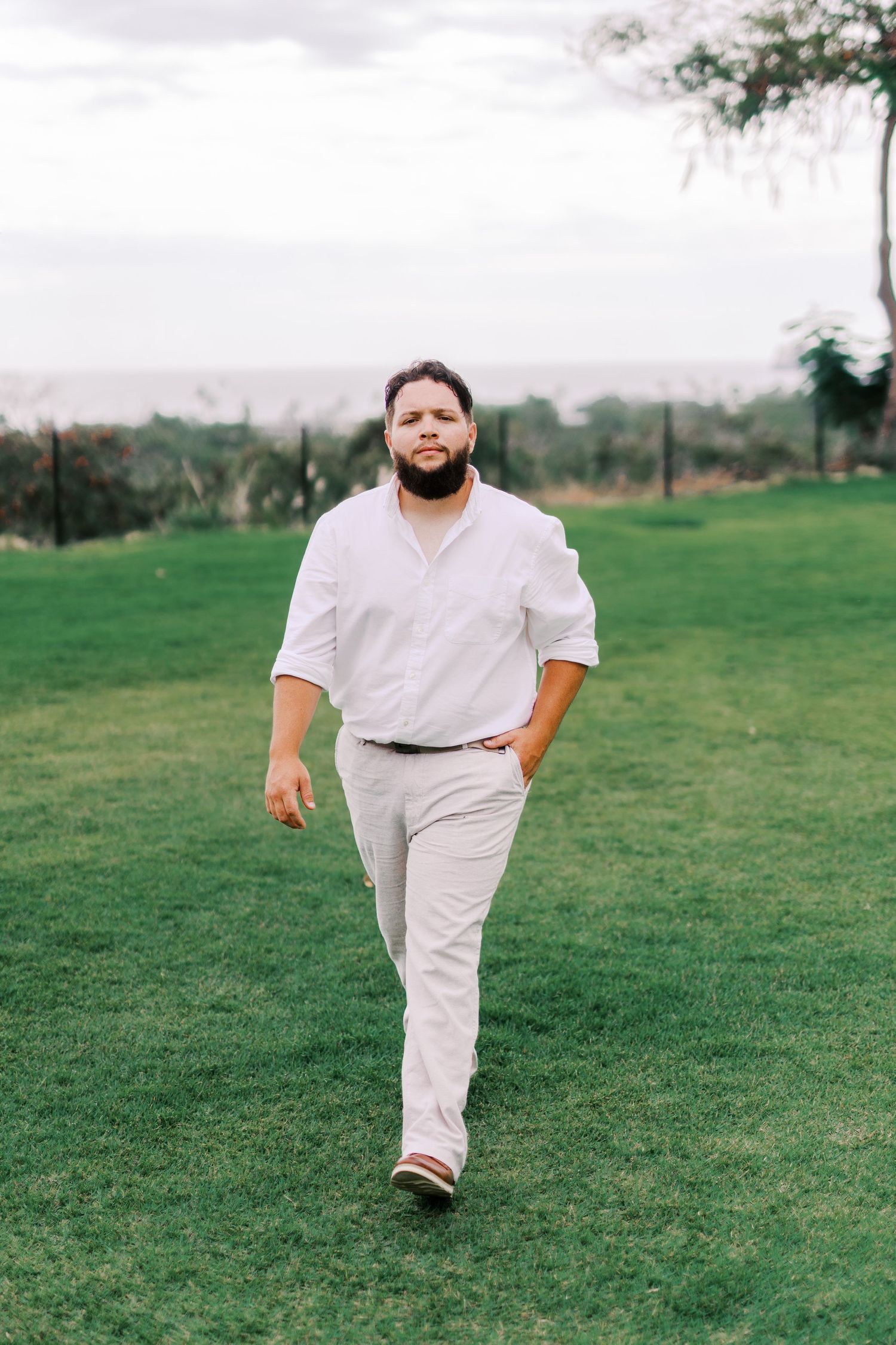 Person in casual white attire walking on green lawn with scenic landscape background.