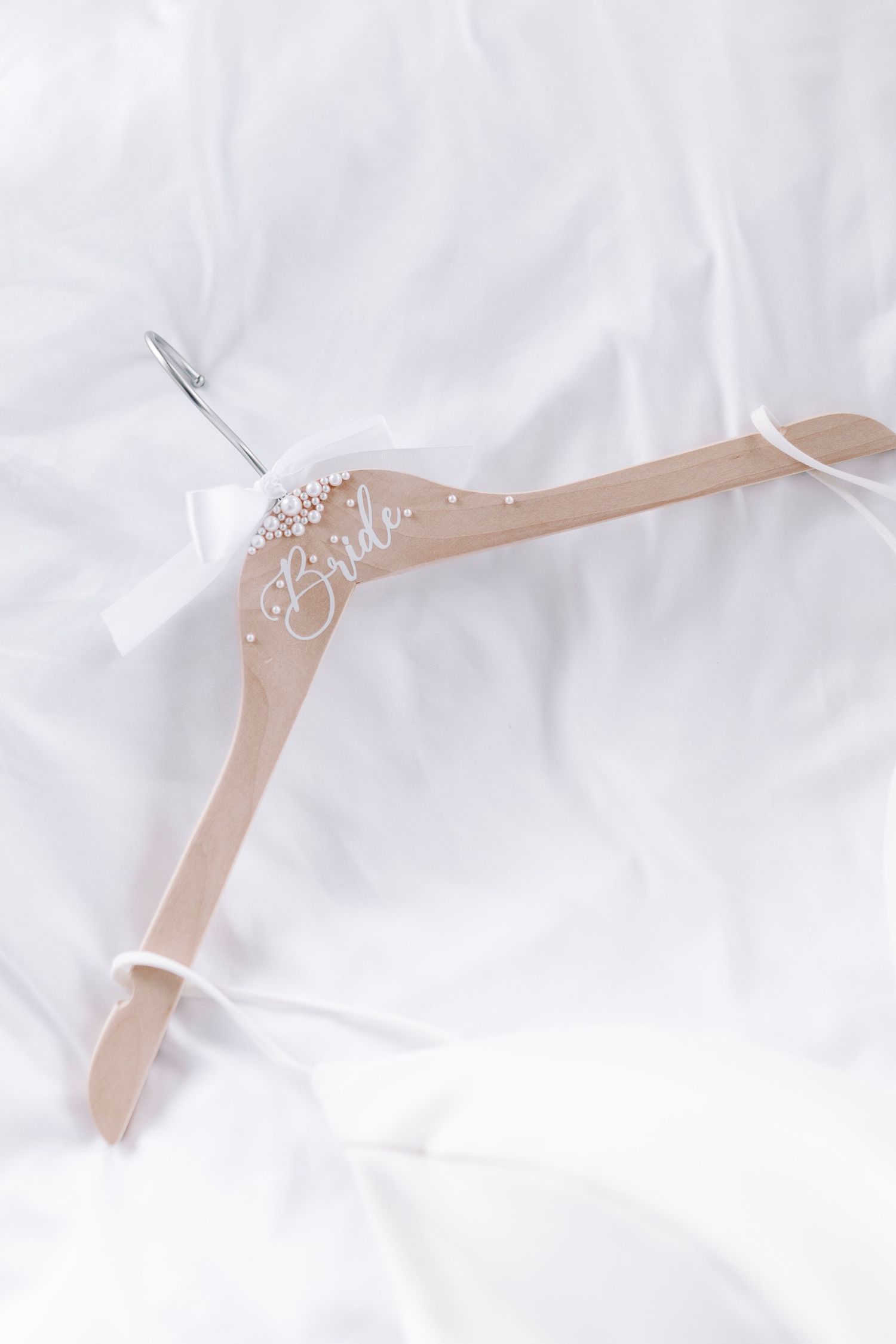A custom wedding dress hanger decorated with pearl and crystal embellishments on white fabric background.