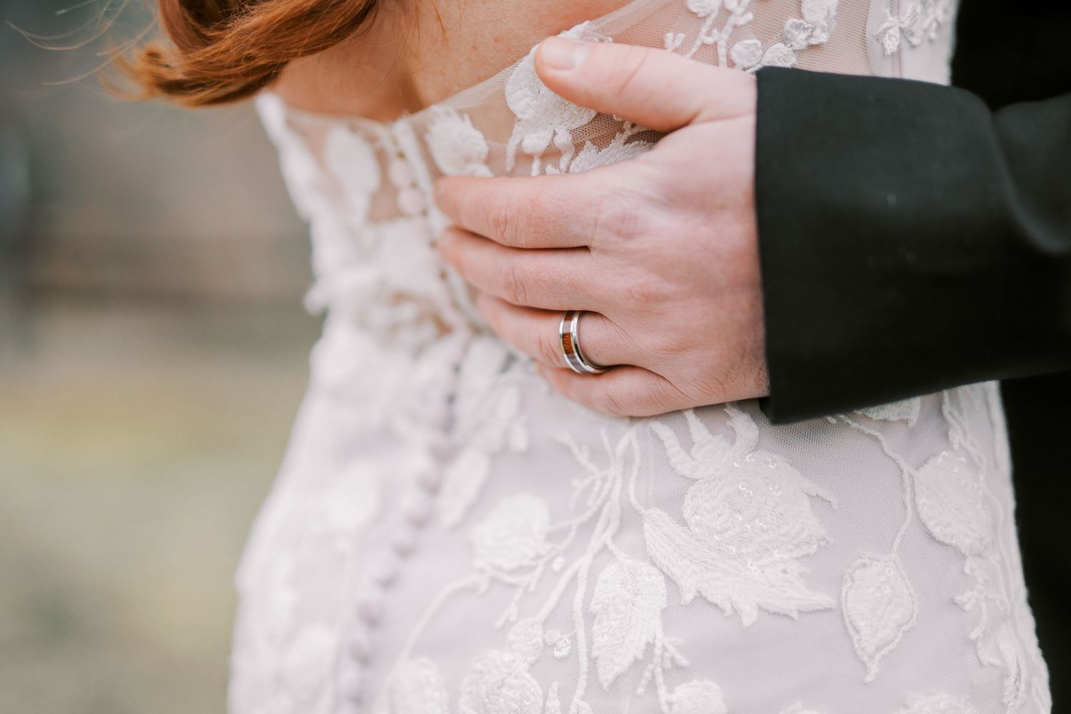 A close-up detail shot of lace wedding dress fabric and engagement ring.