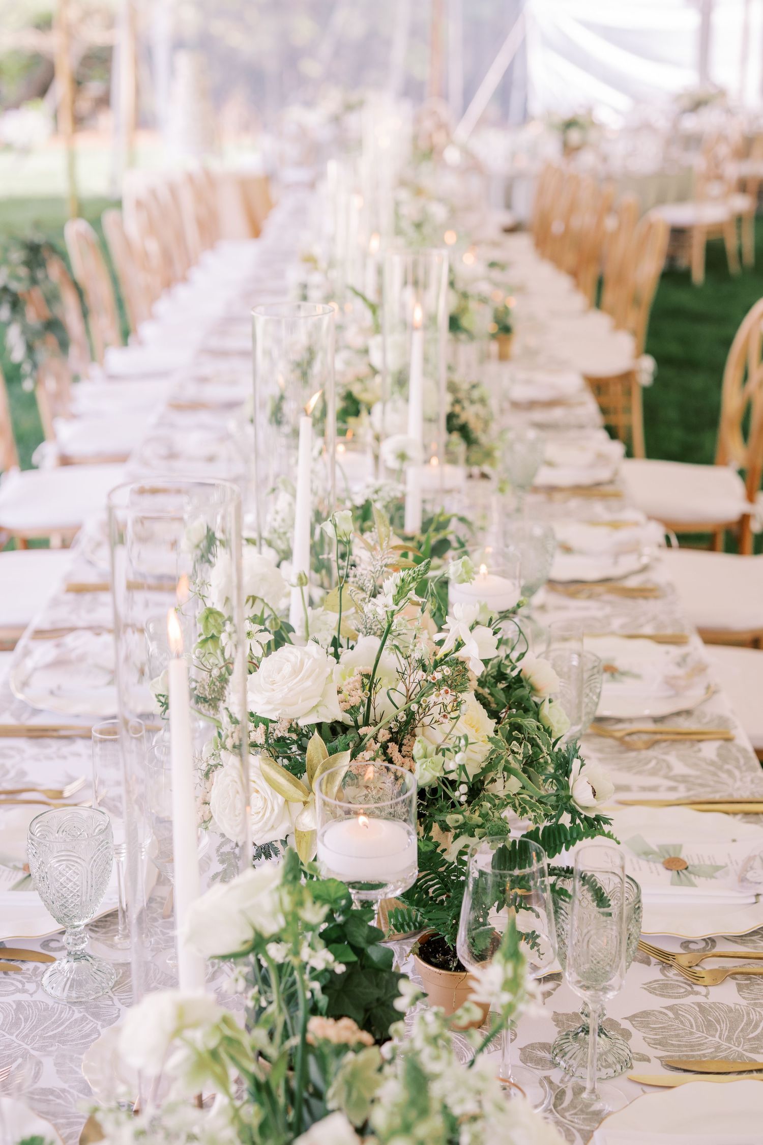 Elegant wedding table setting with white roses, greenery garland centerpiece and tall taper candles on a long banquet table.