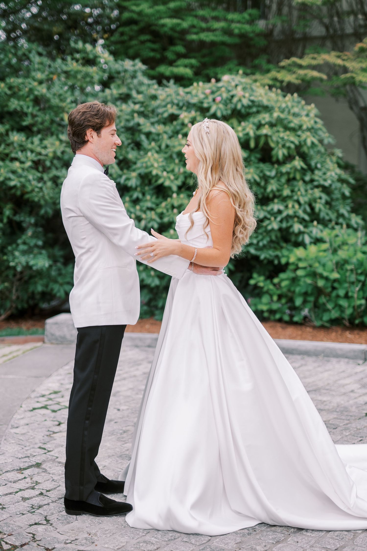 A couple in wedding attire dance together in a peaceful garden setting with lush greenery in the background.
