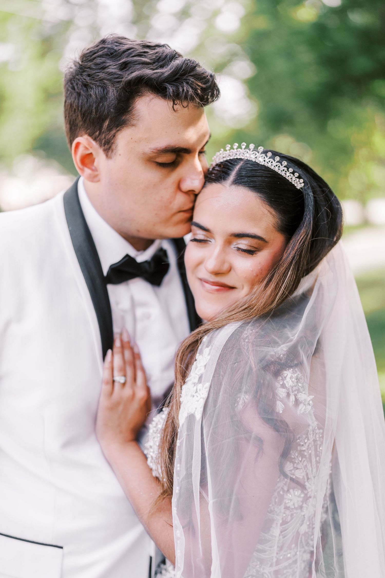 A romantic wedding couple shares intimate moments together through a delicate veil in an outdoor garden setting.
