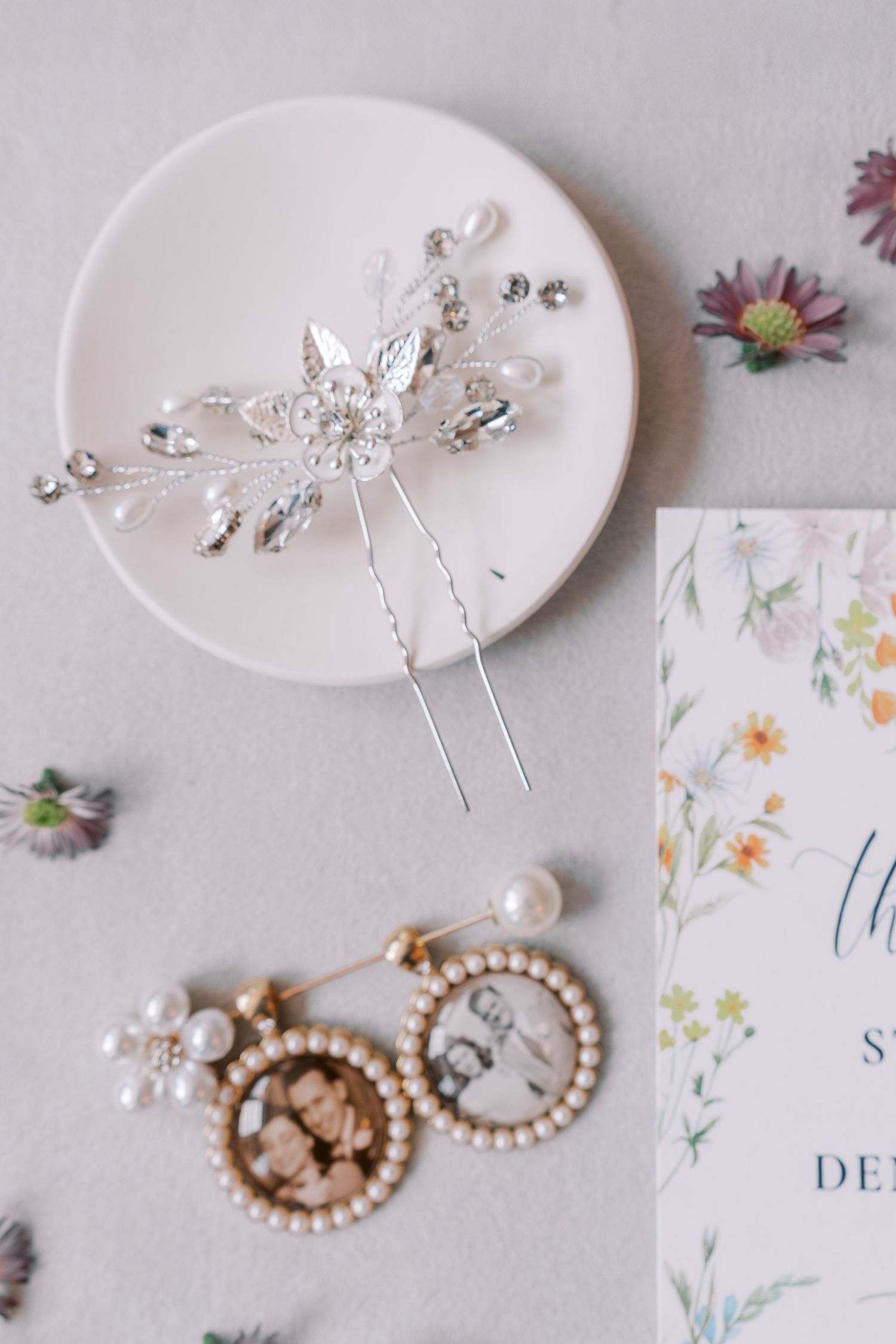 Delicate bridal accessories including silver hairpins and pearl jewelry laid on a floral background.
