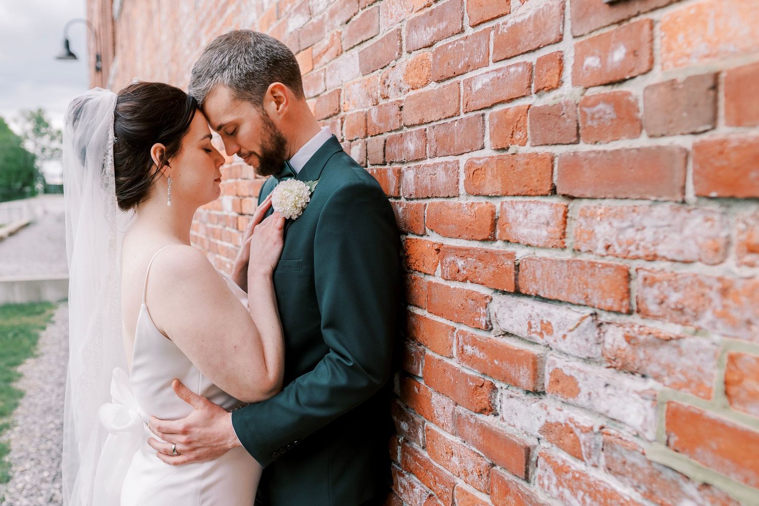 A romantic moment between newlyweds against a rustic brick wall with a delicate veil flowing.