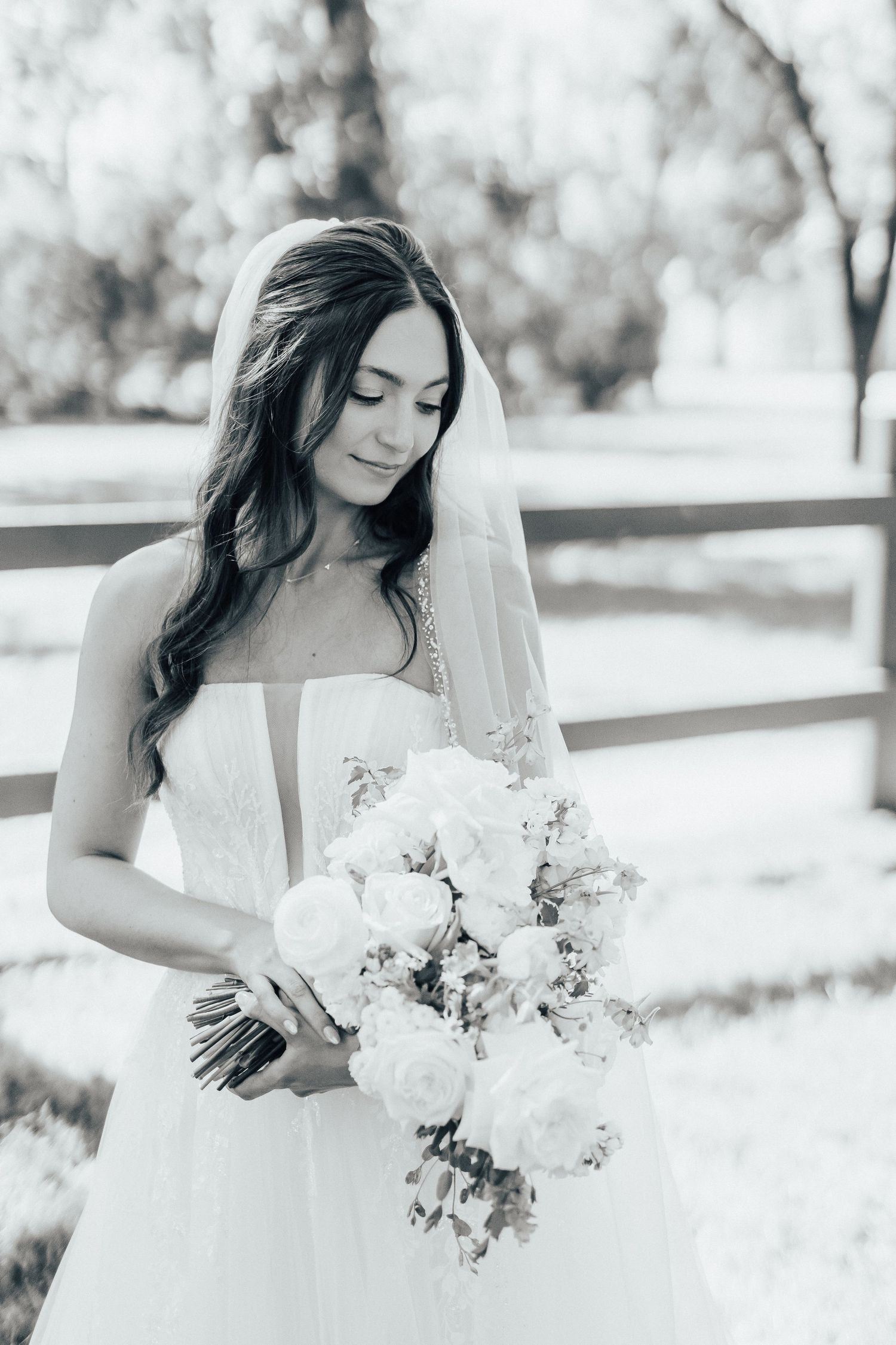 Black and white portrait of a bride in white dress holding a delicate bouquet of flowers in an outdoor setting.