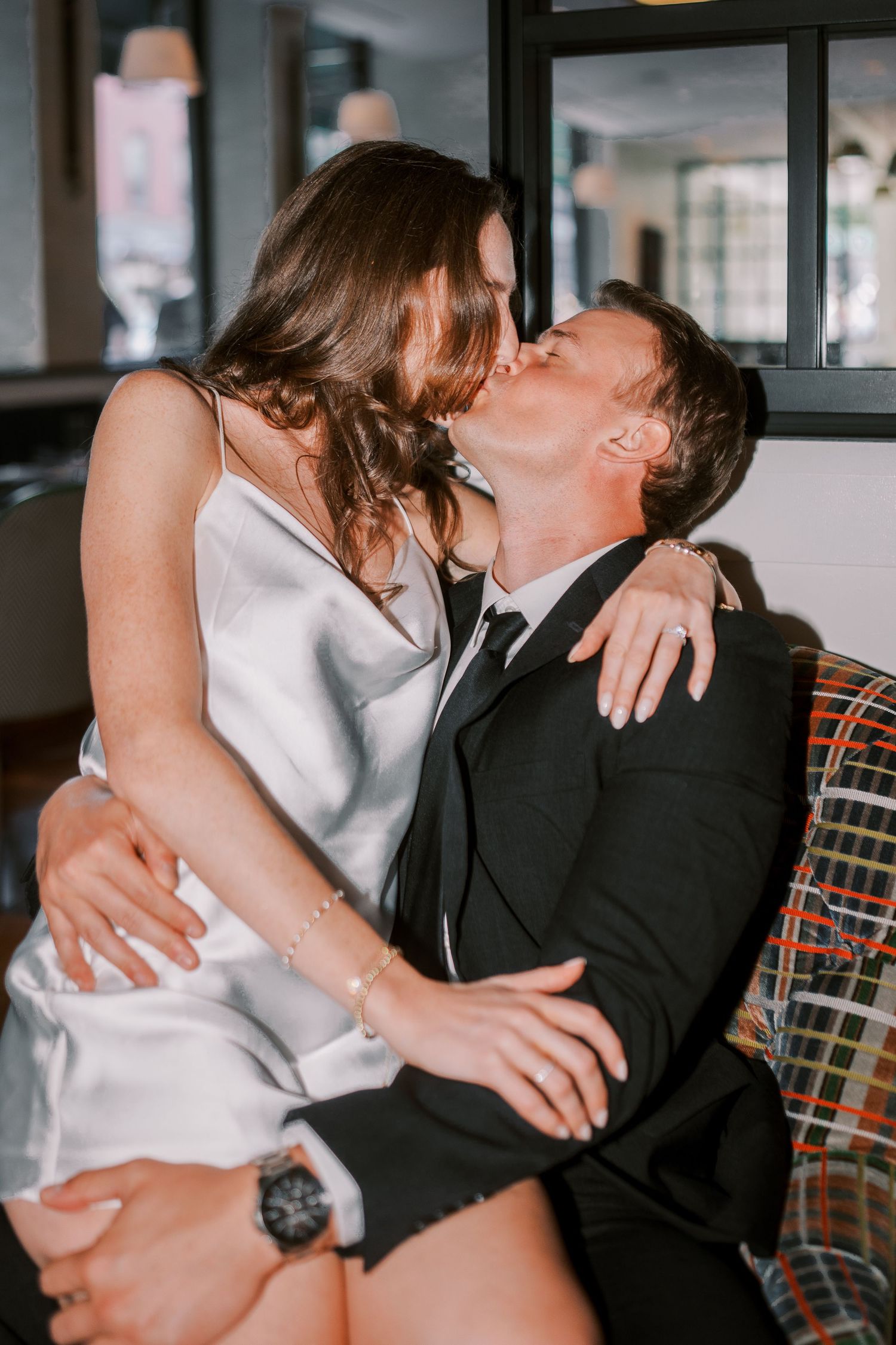 A bride and groom share intimate wedding kisses in an indoor venue with plaid seating.