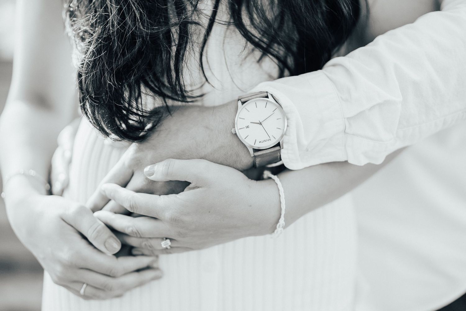 Close up shot of a tender embrace showing hands and a wristwatch against white clothing.