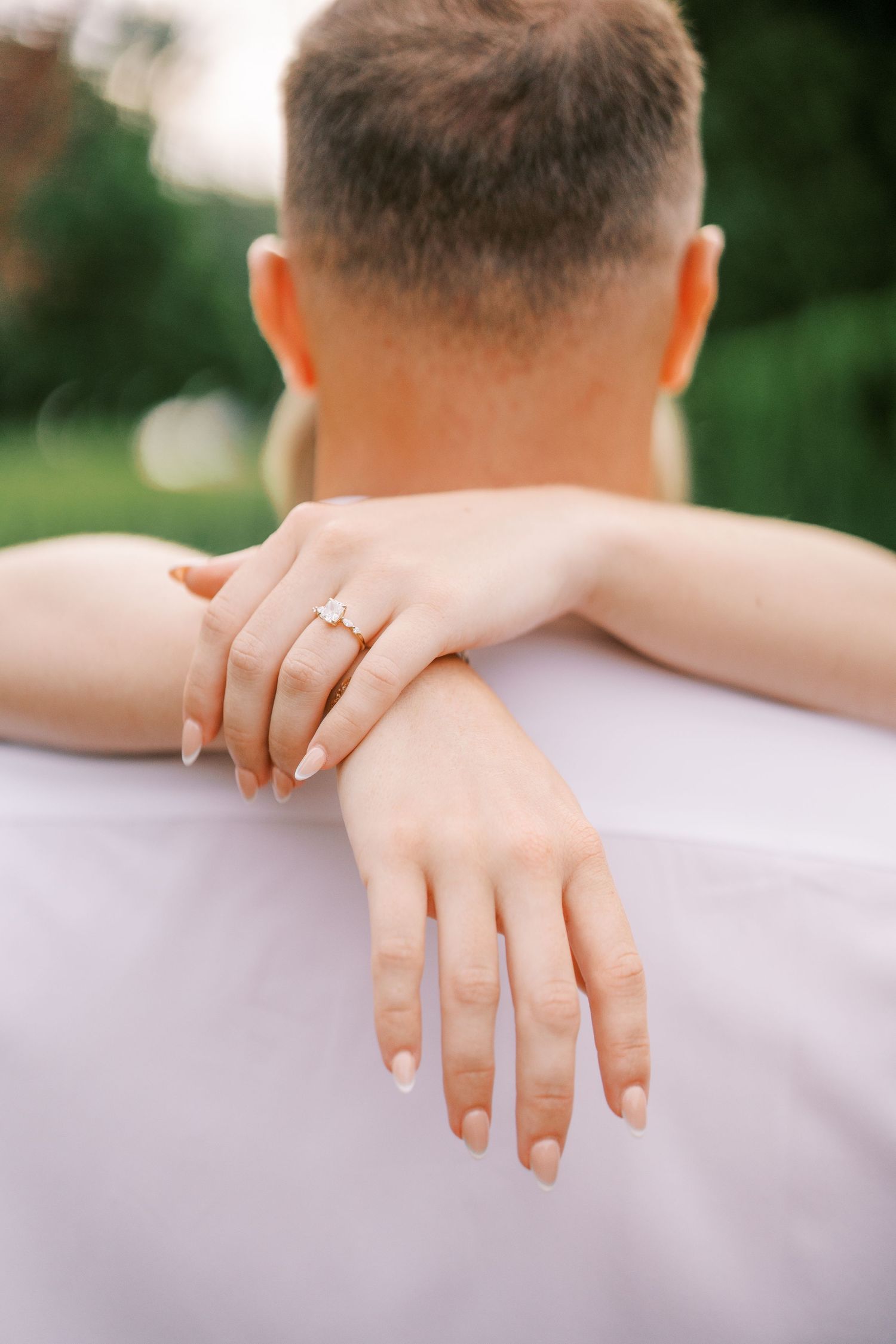 Close up of engagement ring as hands embrace on sunny day.