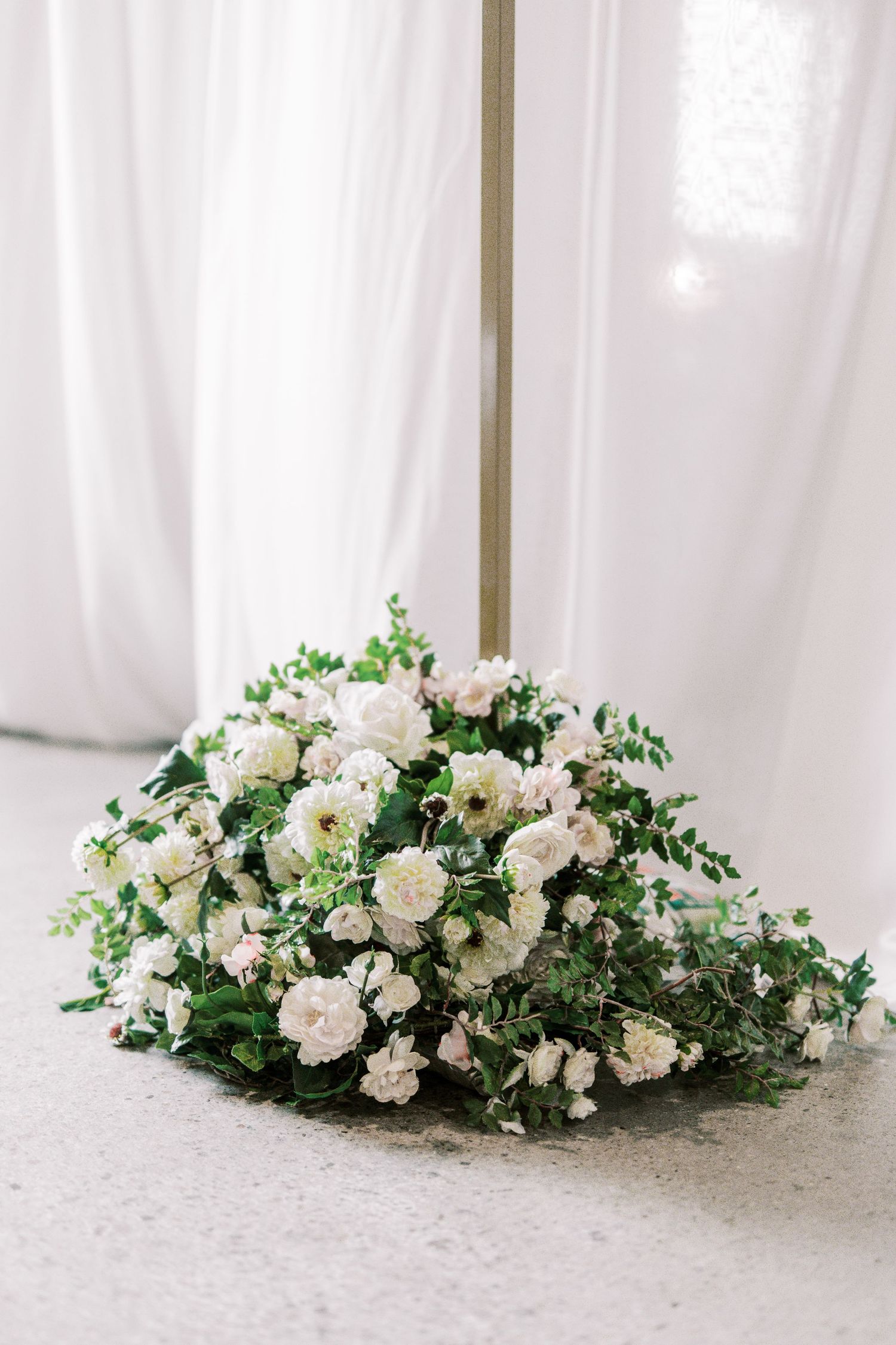 Lush white and green floral arrangement with roses and delicate greenery on light surface.