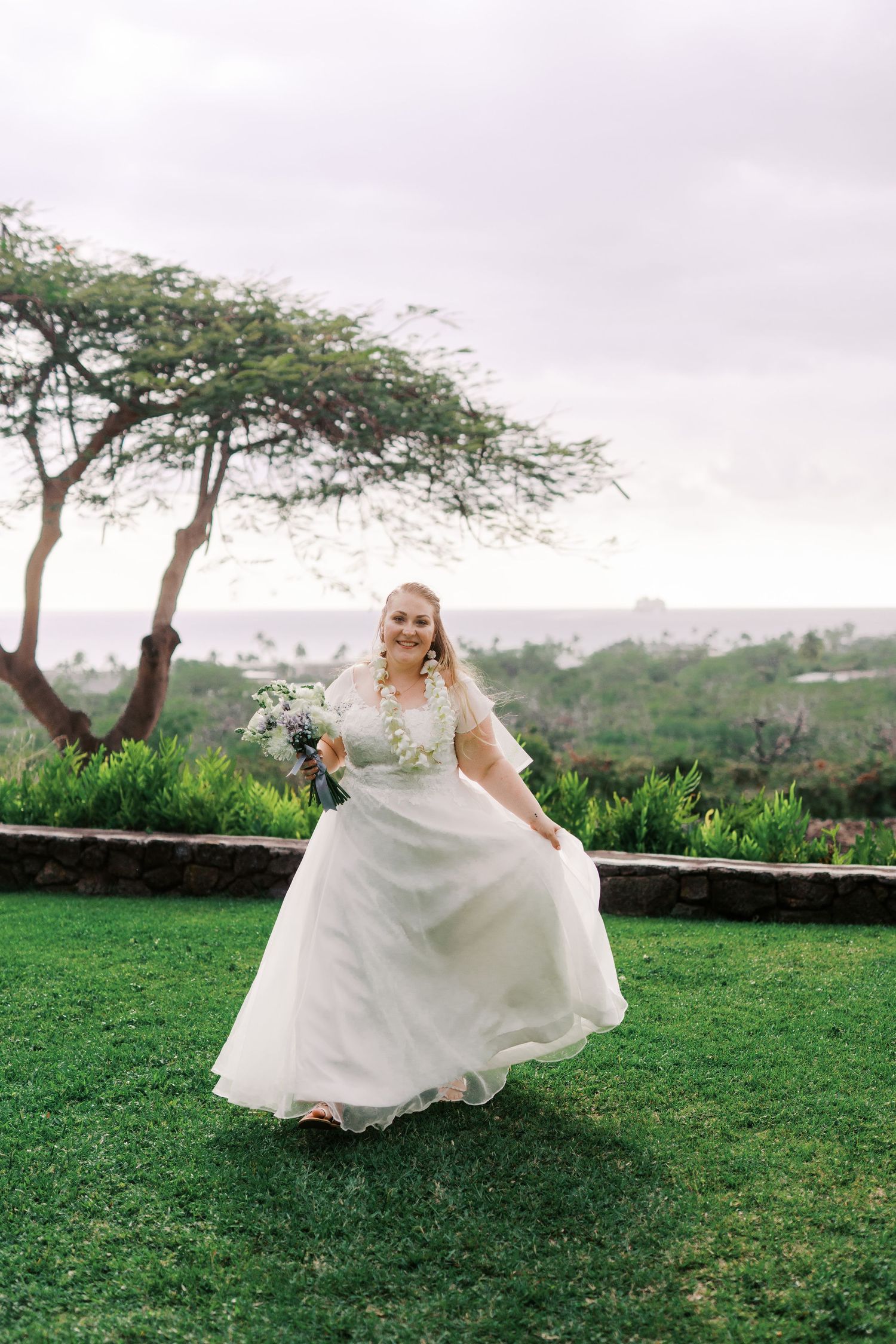 Wedding dress flowing in breeze on green lawn with scenic overlook.