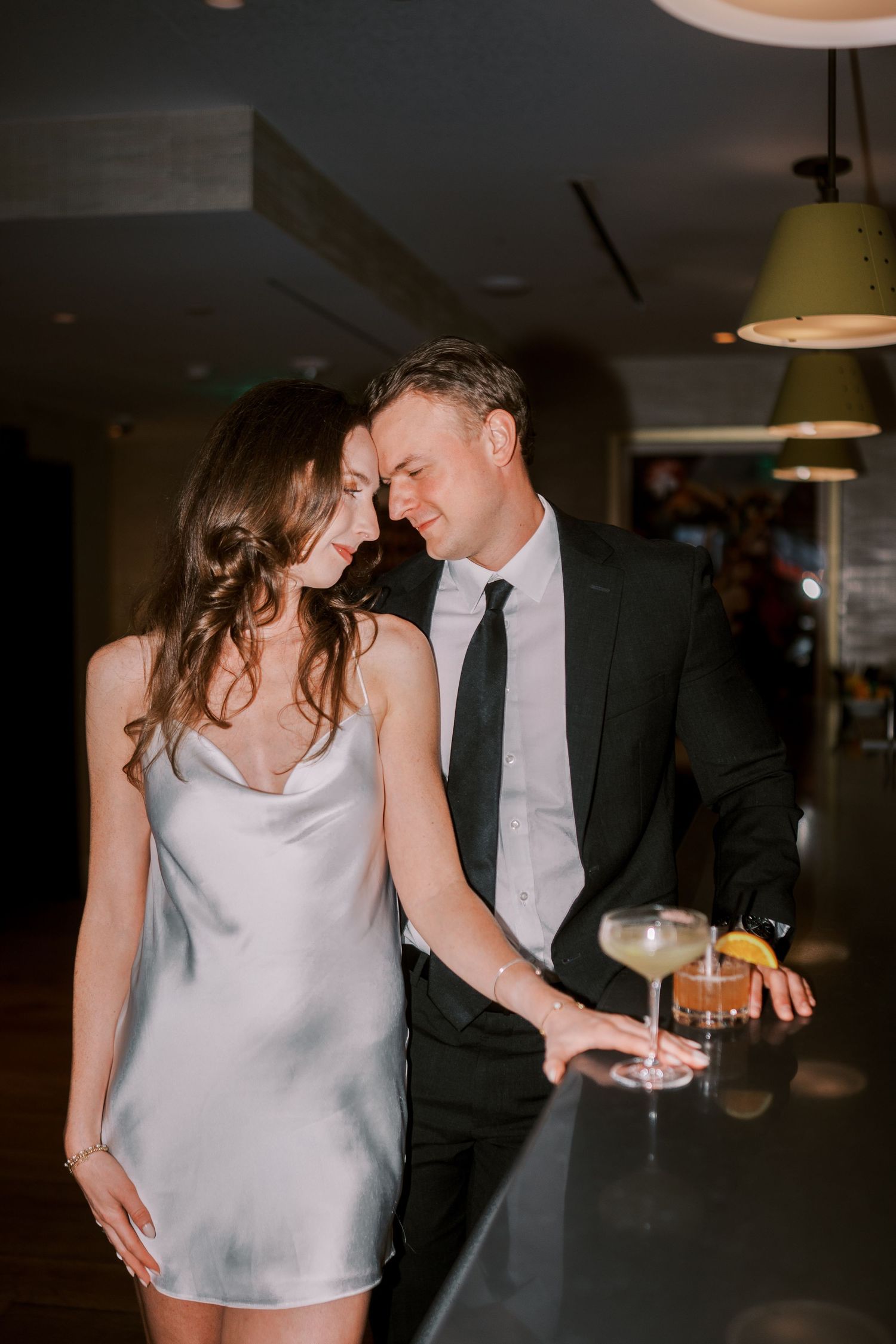 Elegant couple in formal attire sharing drinks and an intimate moment at an upscale bar.