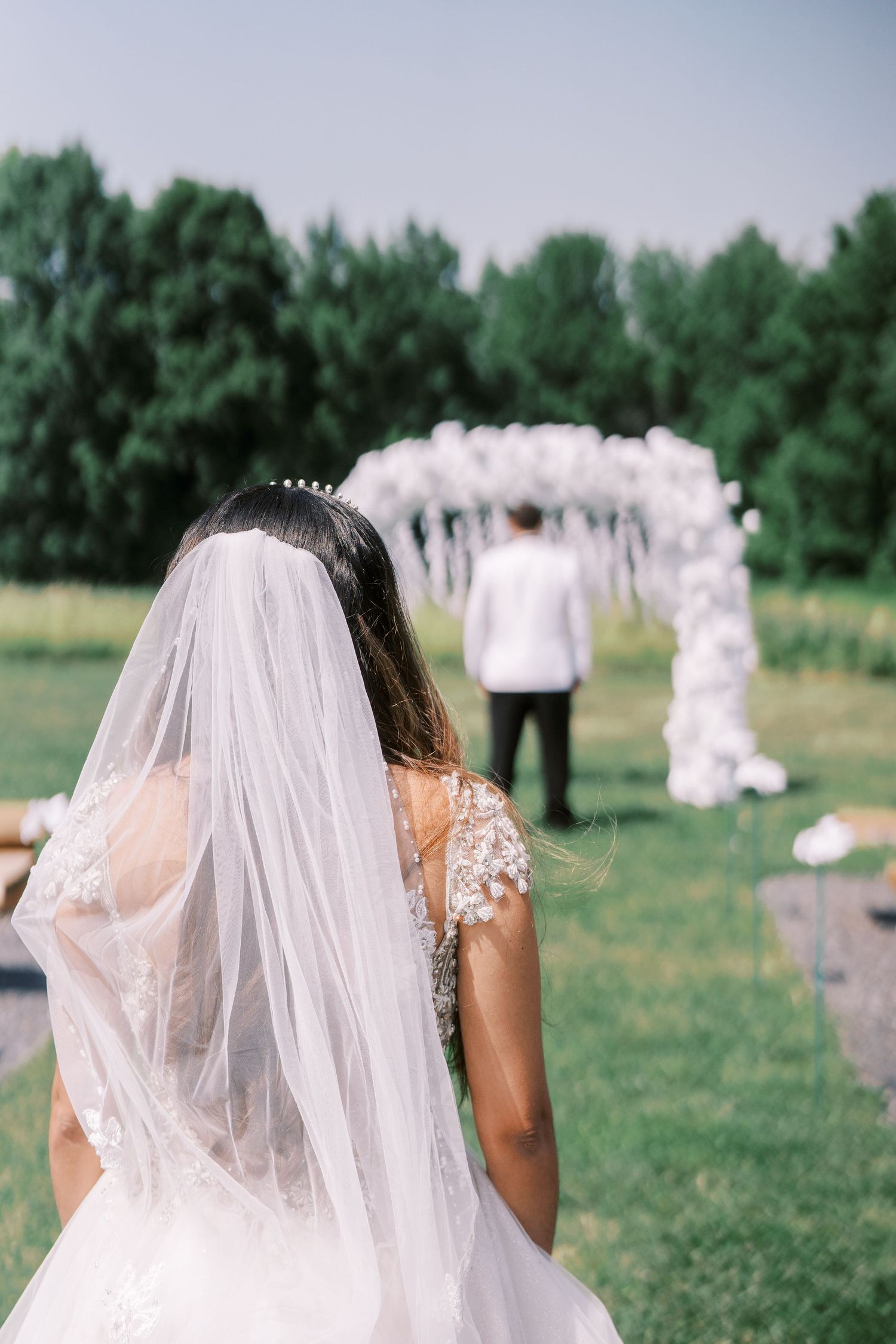 Beautiful outdoor wedding ceremony setup with floral arch and bride in flowing veil looking towards decorated altar.