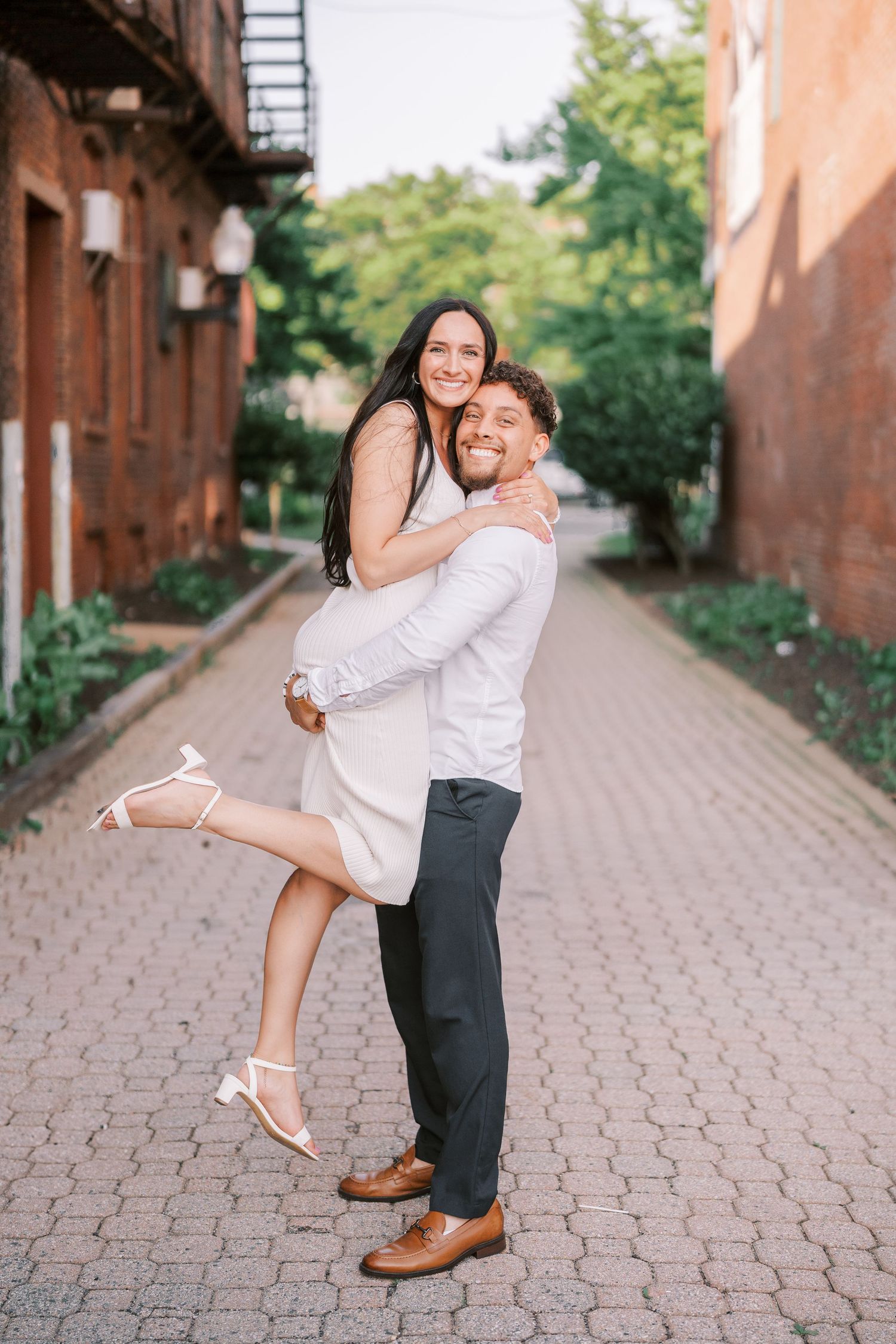 A couple plays and laughs together on a brick-paved pathway.