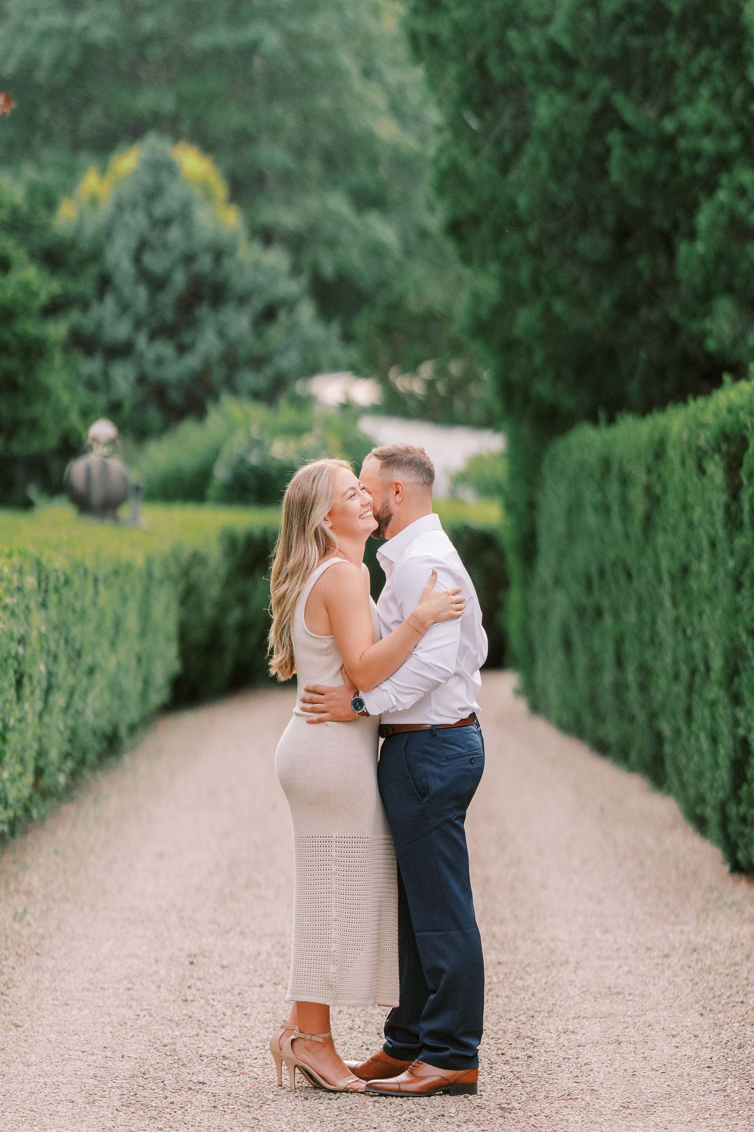 Romantic couple embraces on a garden path surrounded by manicured hedges and lush greenery.