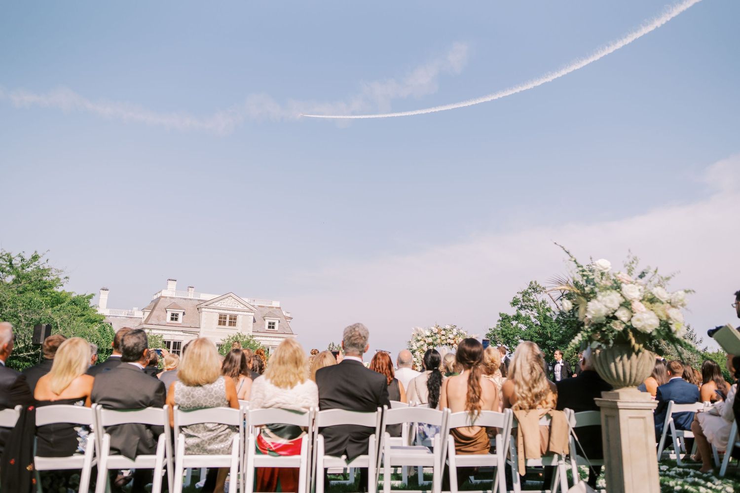 Row of wedding guests raising their hands in celebration during an outdoor ceremony under blue sky.