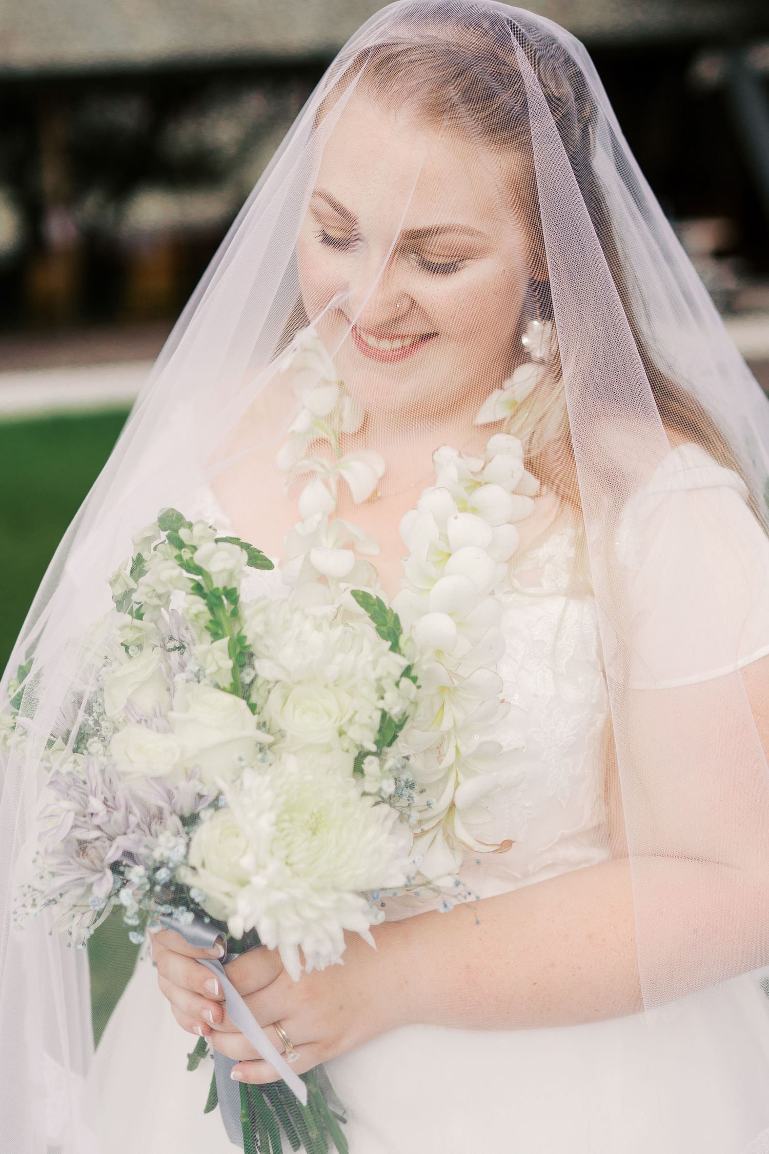 Bride holding elegant white and green bouquet wearing traditional veil.